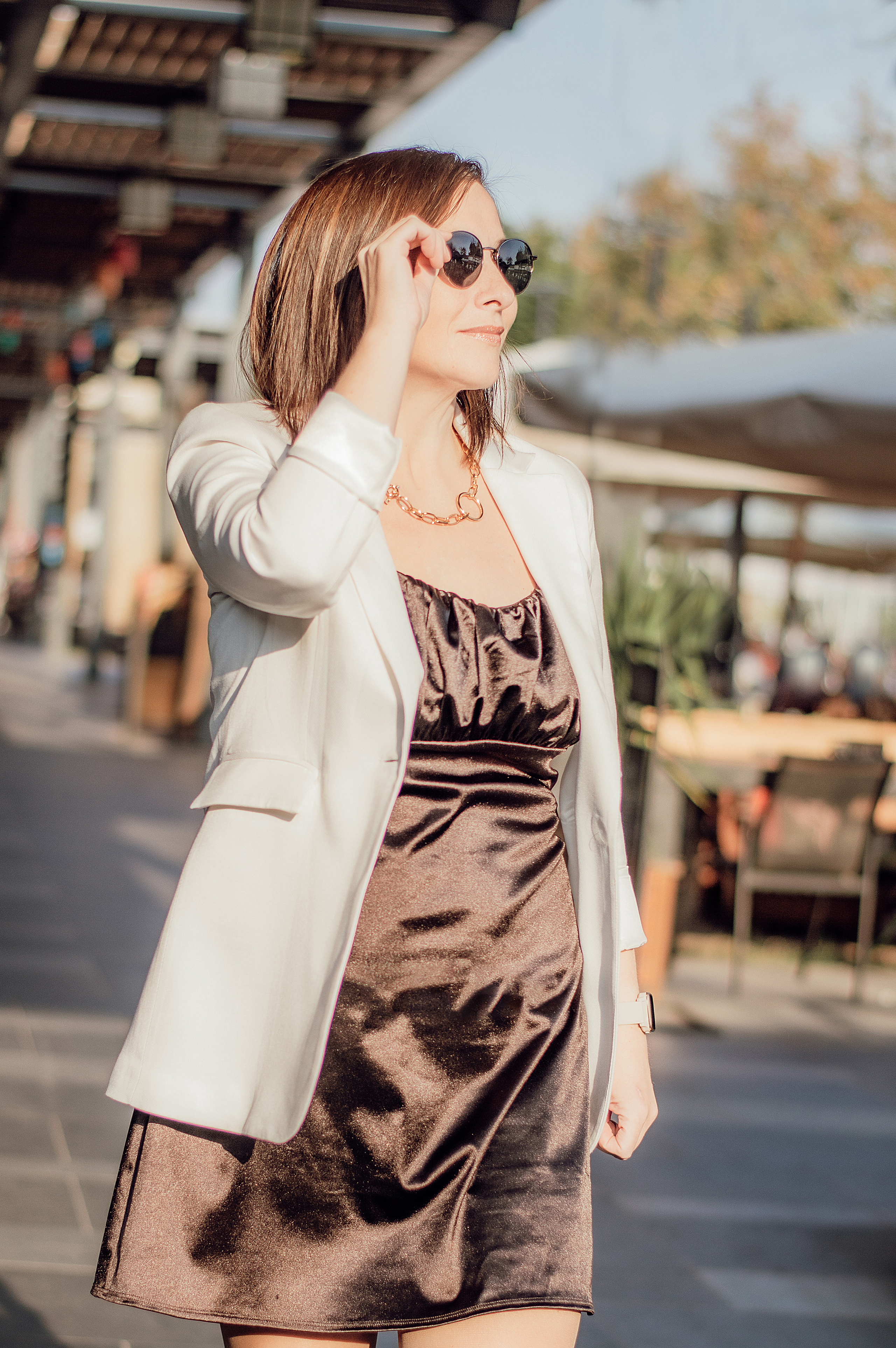 девушка в белом пиджаке идет и держится за очки бизнес леди