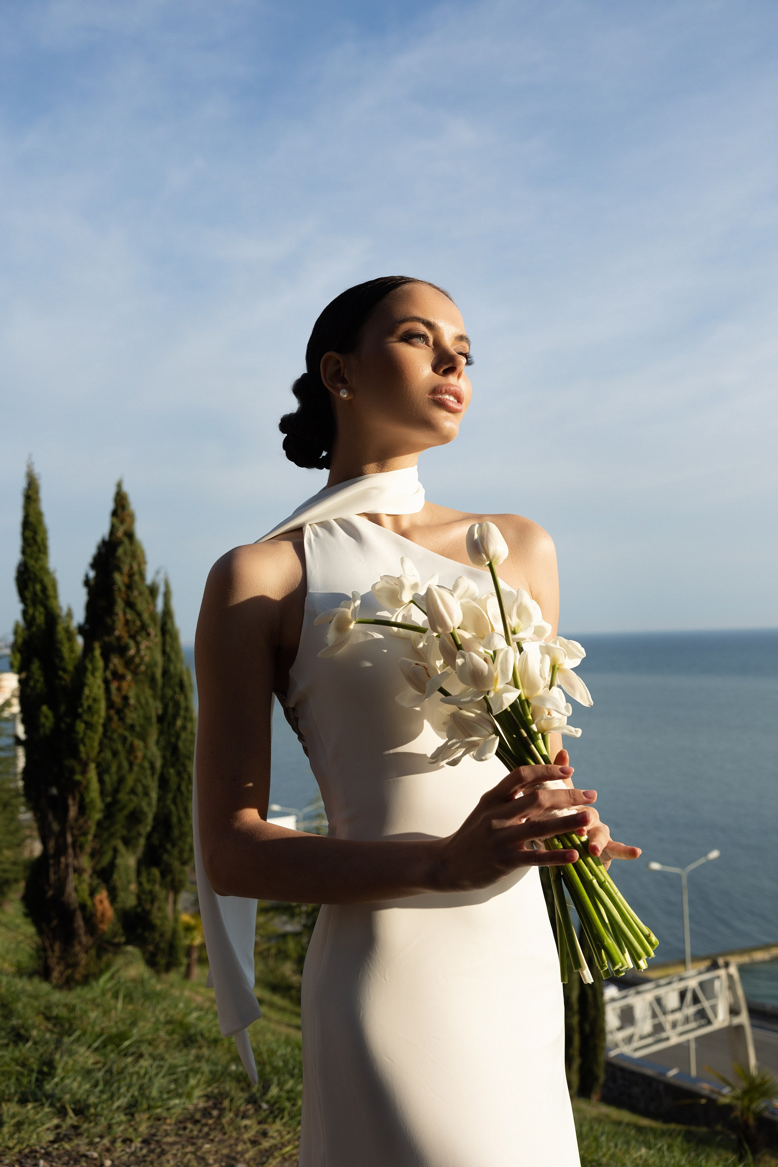 девушка в белом платье держит в руках цветы на фоне моря