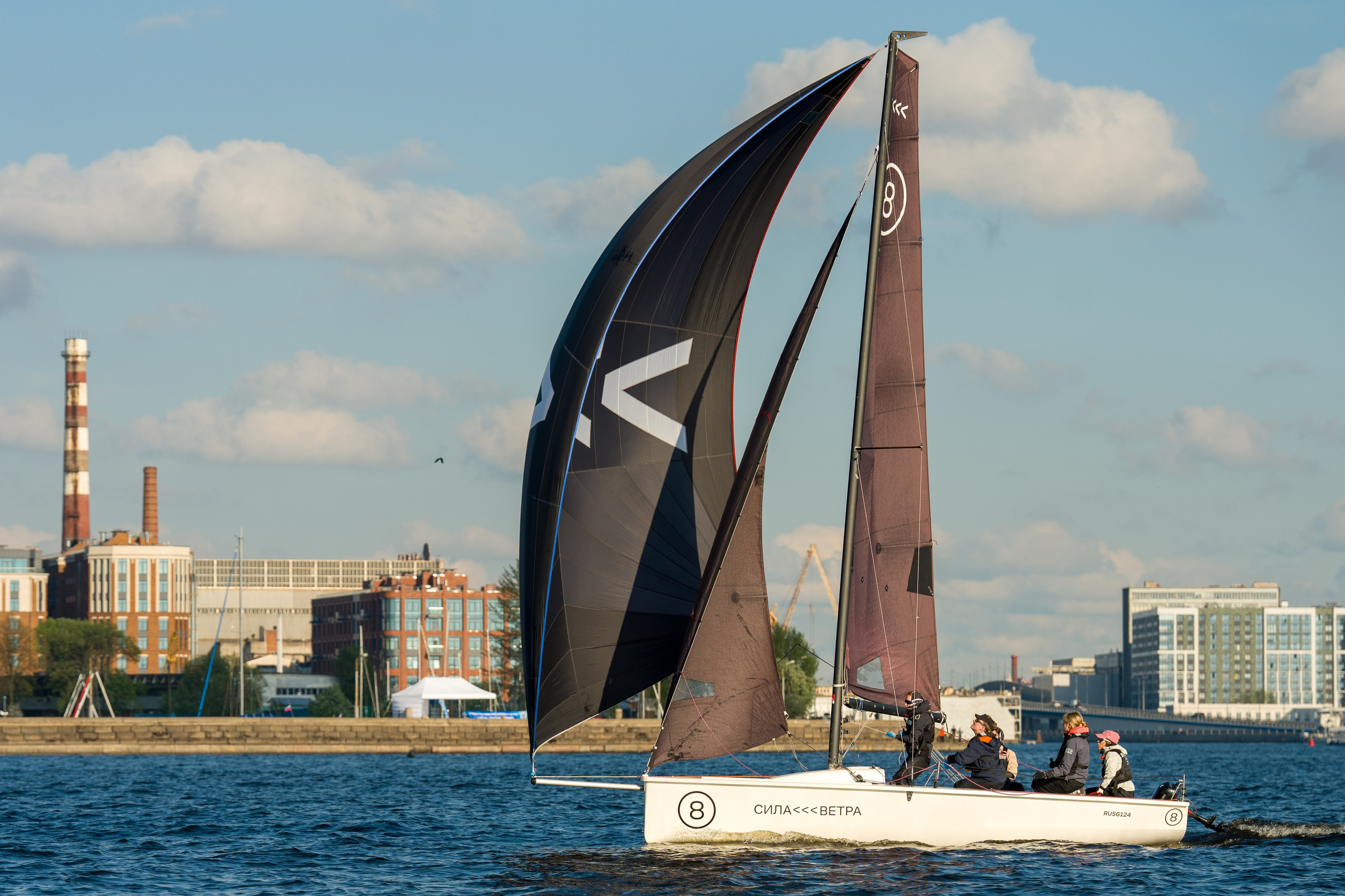 SV20 crew trims sheets on pace, sunny waterfront skyline behind