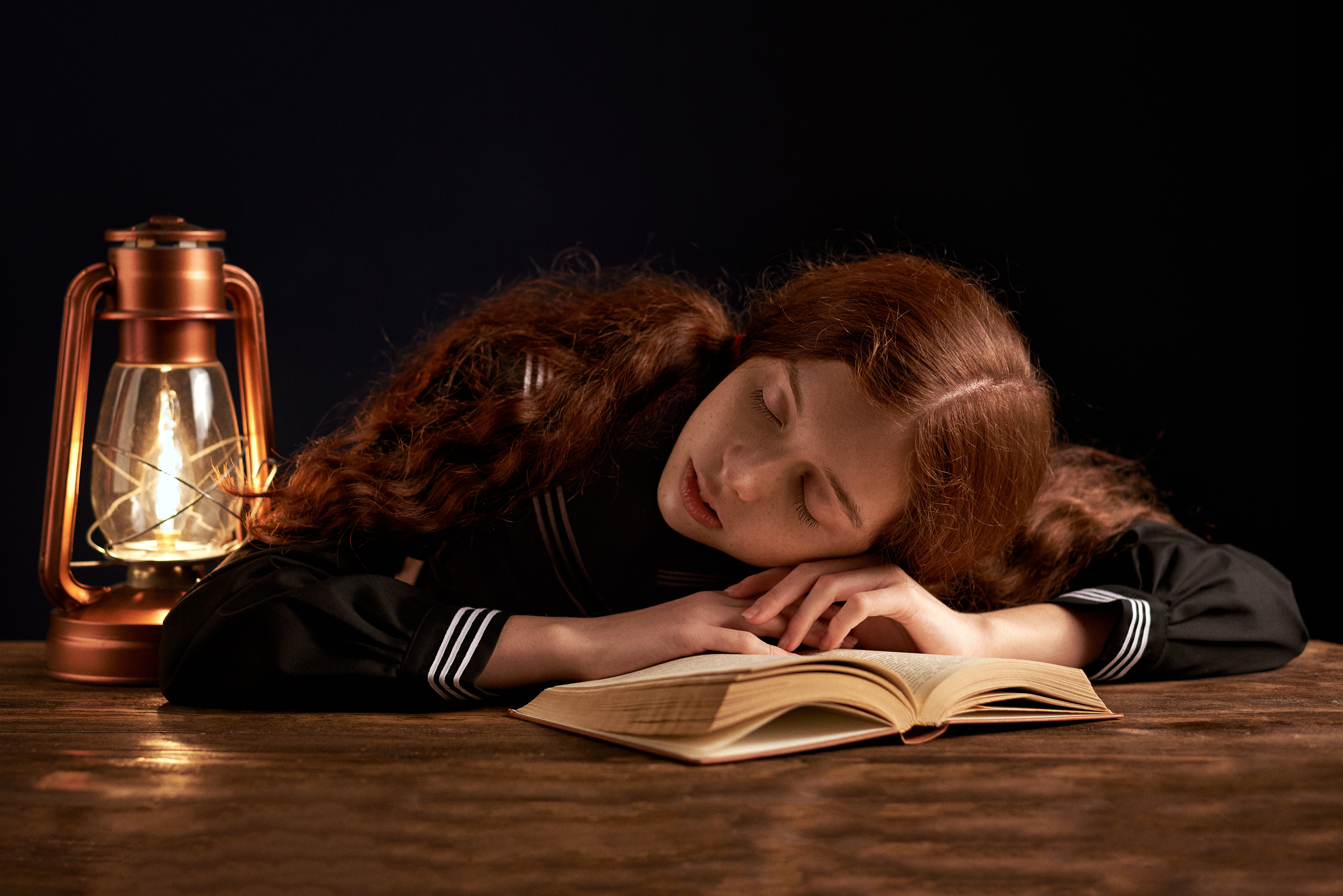 Девочка-подросток задремала за чтением любимой книги при свете керосиновой лампы 