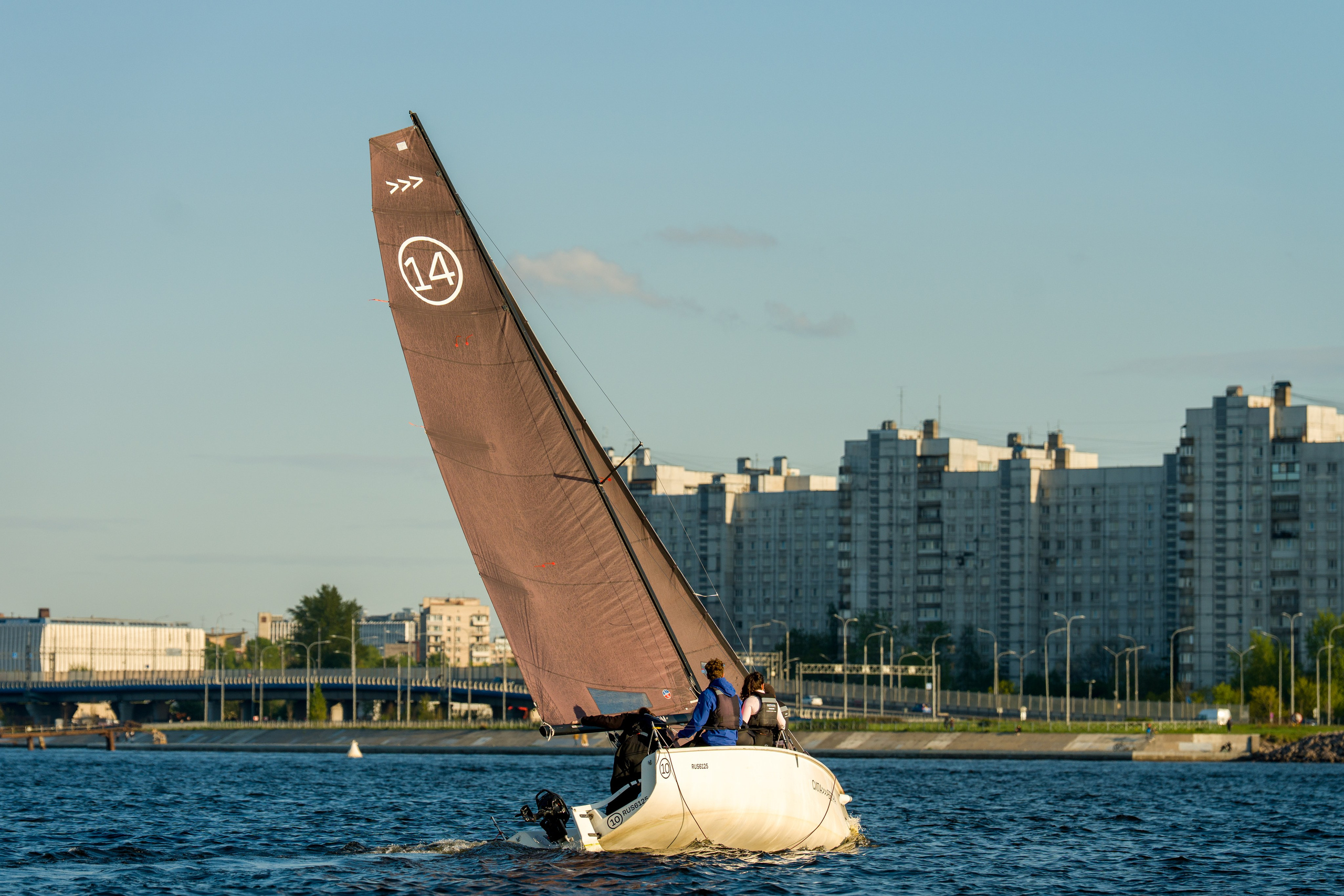SV20 crew trims sheets, sailing past bridge with city skyline