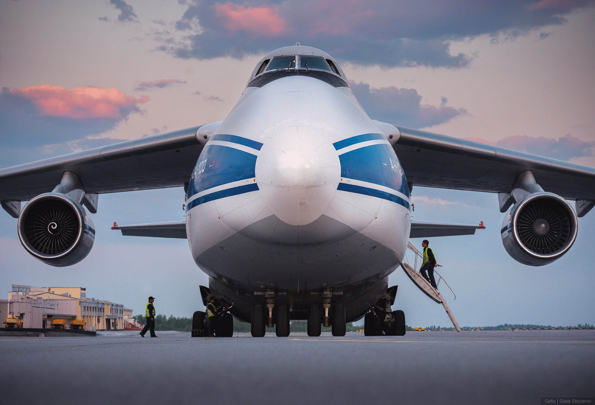 Фронтальный ракурс тяжелого дальнего транспортного самолета Ан-124 «Руслан» авиакомпании «Волга-Днепр» на летном поле. На встроенном трапе и у шасси находится технический персонал. Снимок Gelio.