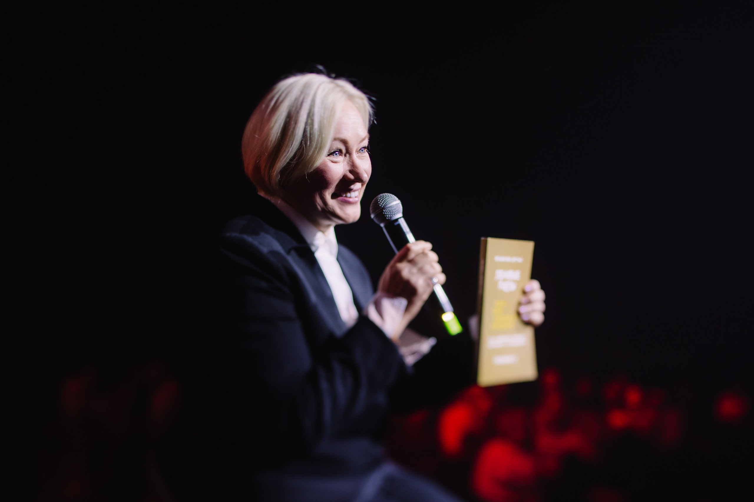 Награждение/Вручение: Владислава Друтько с микрофоном и собственной книгой в руках, фиксация важных моментов признания и успеха.