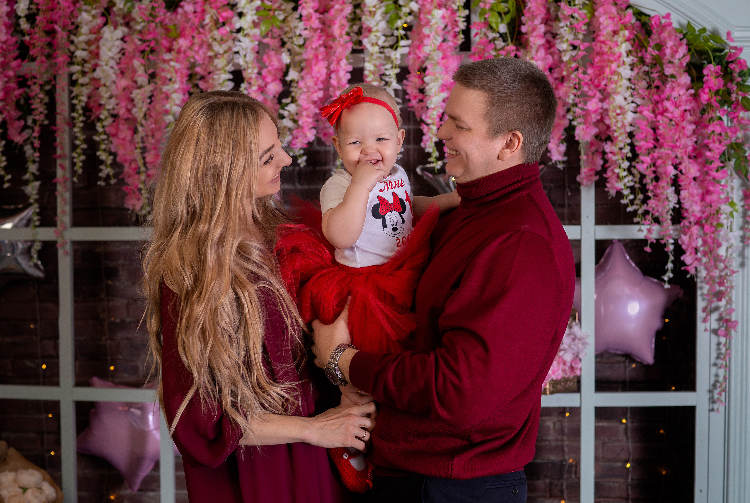 Счастливые родители с маленькой дочкой на фоне весенних цветов свисающих сверху.