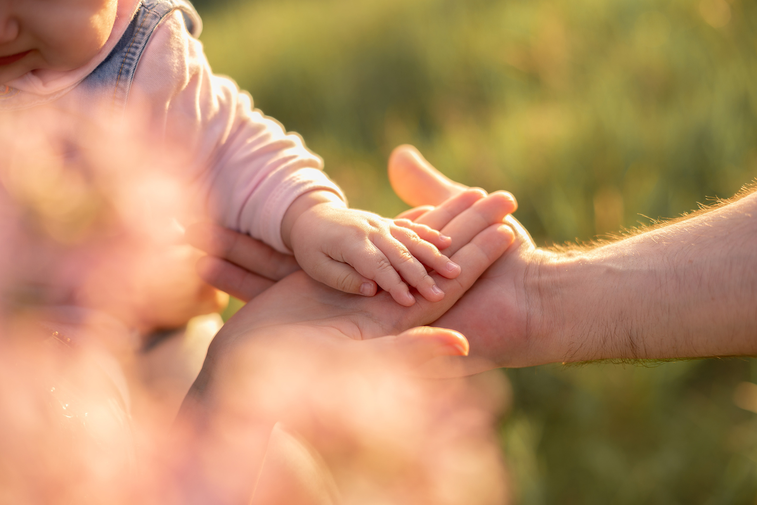 Руки родителей и ребенка крупным планом освещенные лучами заката, всё это в фотосессии в Энгельсе.