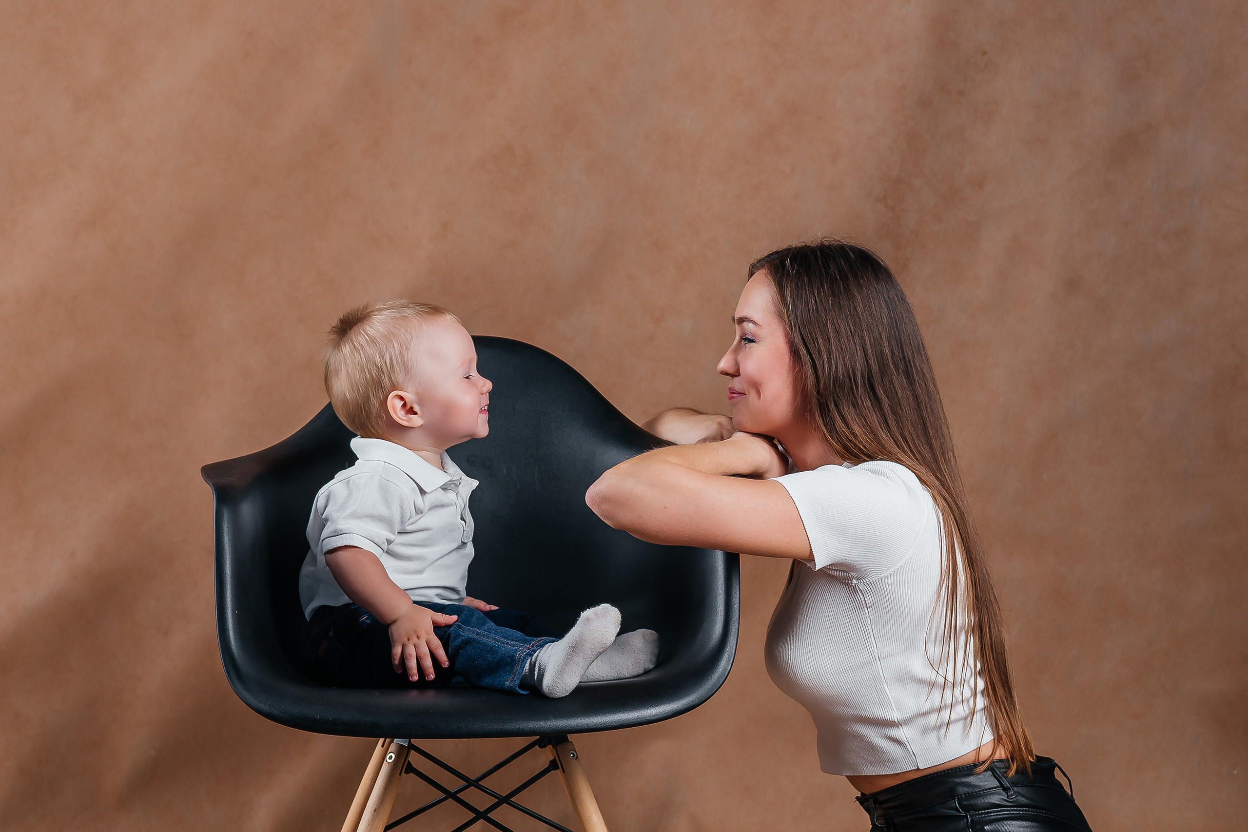 Мать смотрит на сына, который сидит в стильном кресле, а он смотрит на неё. 