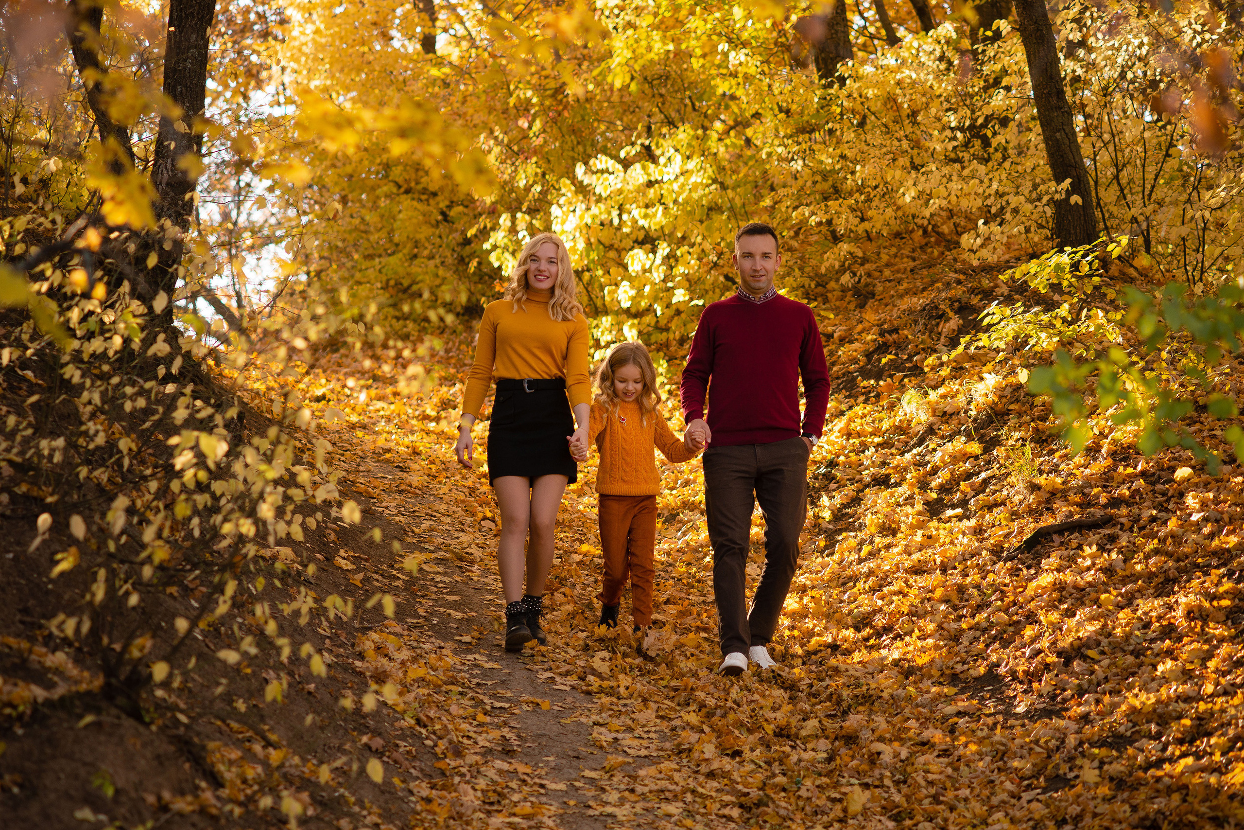 Мама и папа держат с разных сторон дочку и спускаются вниз по склону в осеннем лесу около турбазы Ударник в Саратове.