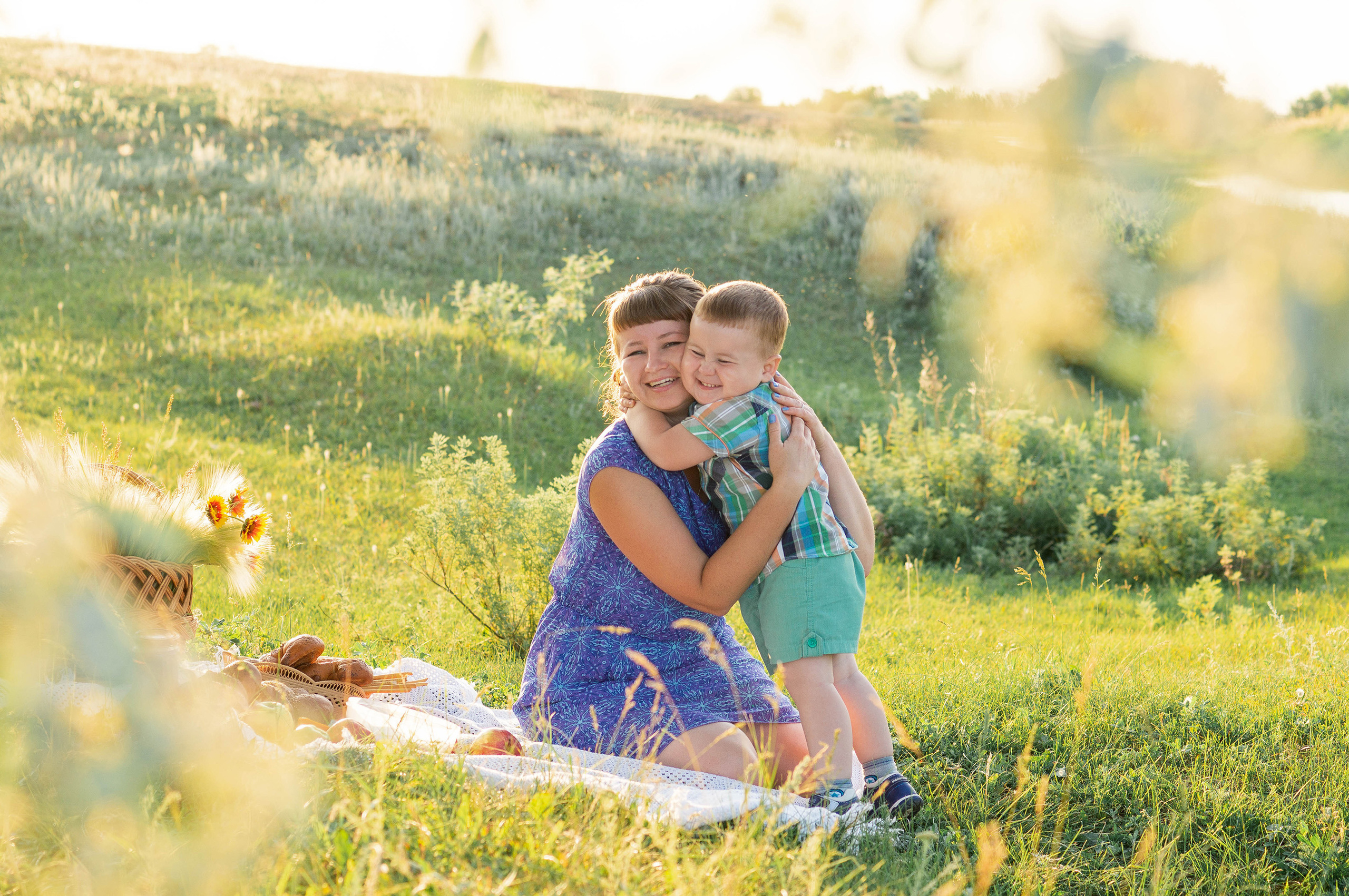Мать обнимается с сыном на фоне зеленого склона освещенного закатным солнцем.