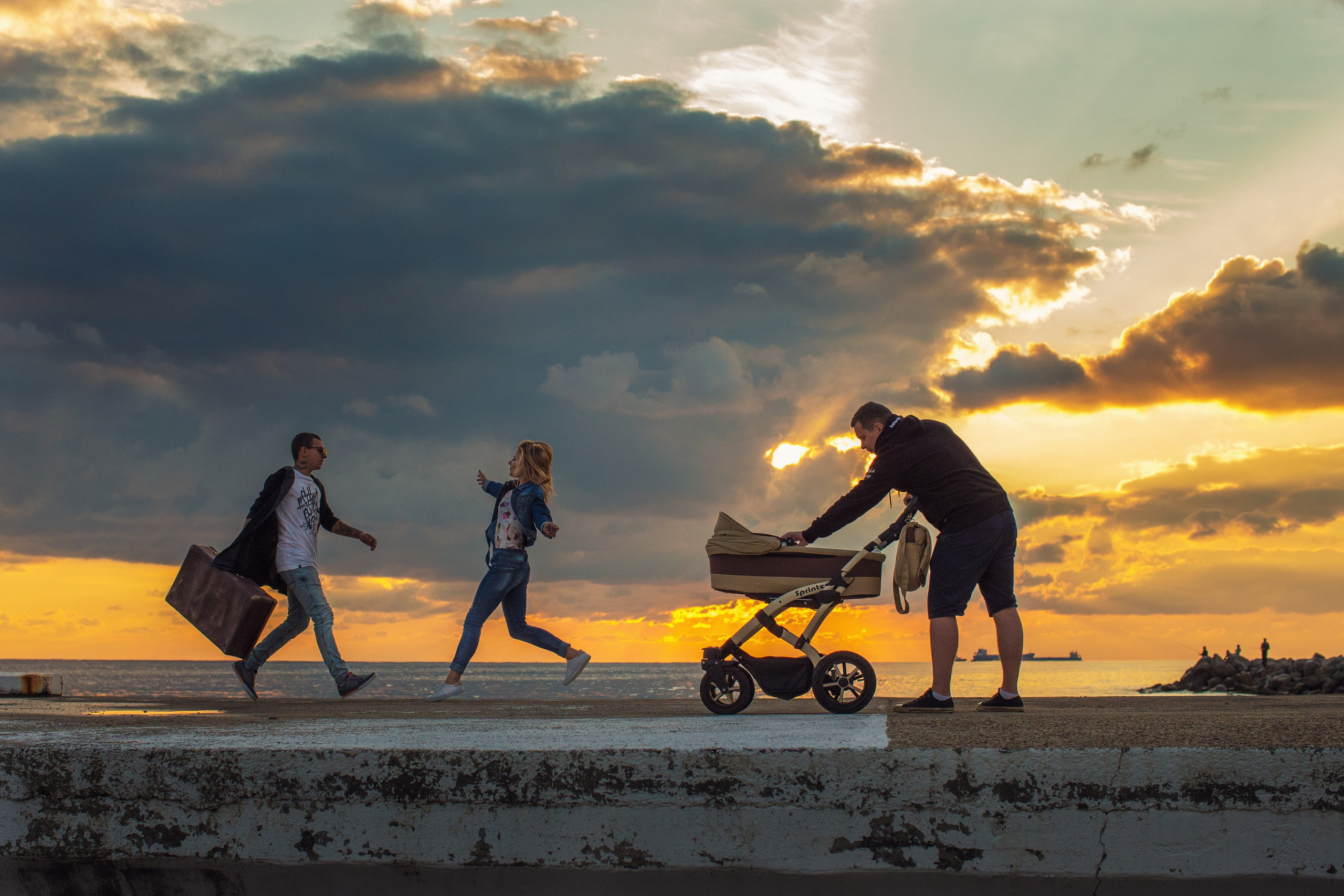 вид на морской причал на котором встречаются влюбленные. парень и девушка бегут по волнорезу на встречу. молодой отец с коляской на причалею красивый закат 