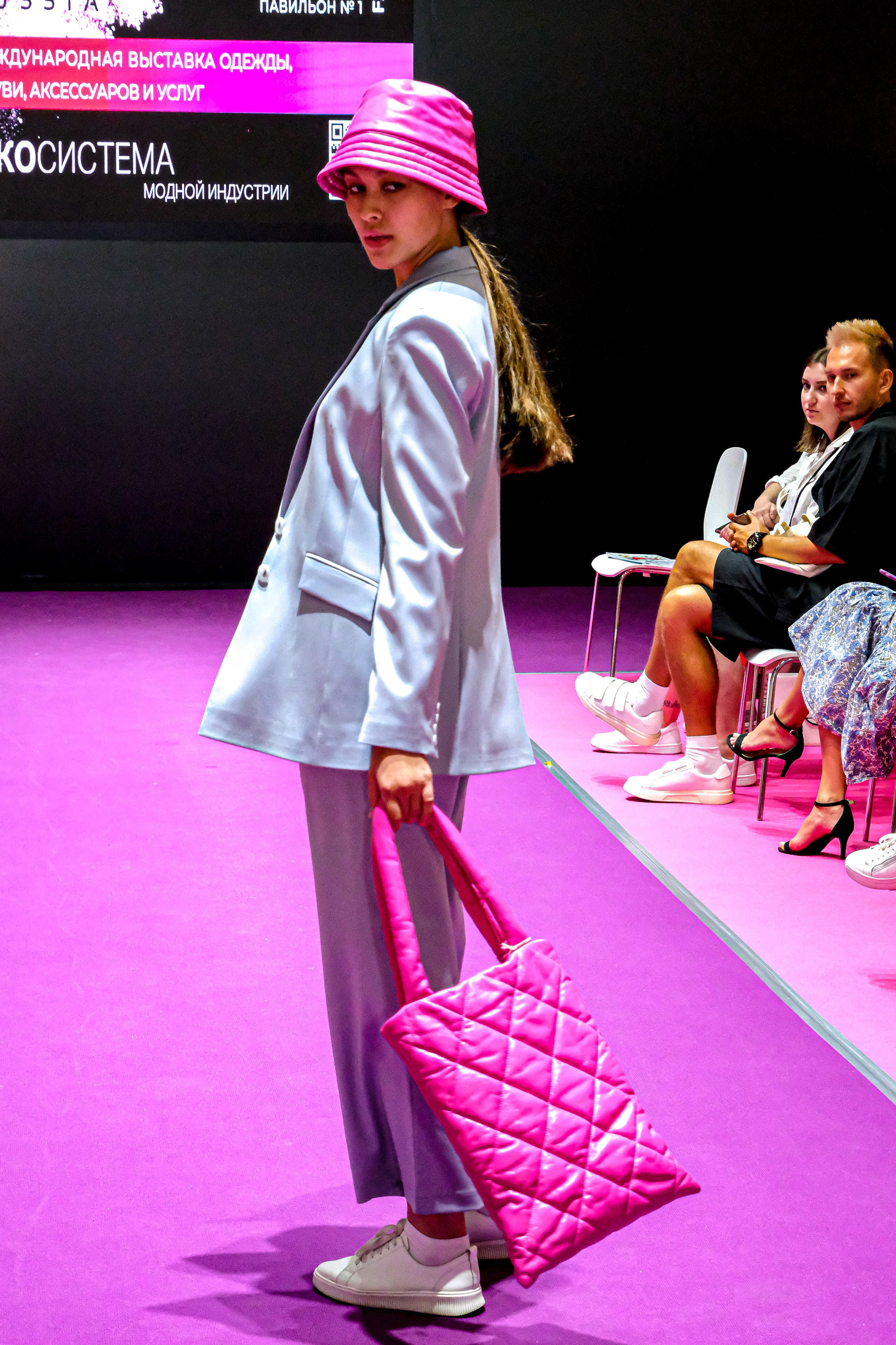  "Модели в ярких нарядах проходят по подиуму во время показа мод, освещенные яркими софитами и окруженные восторженными зрителями."