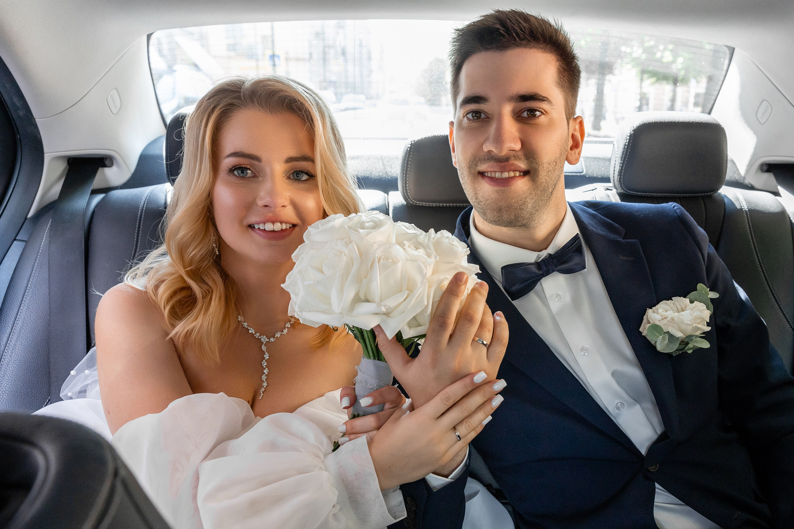 Счастливые молодожены едут в машине на прогулку по городу и демонстрируют свои обручальные кольца
