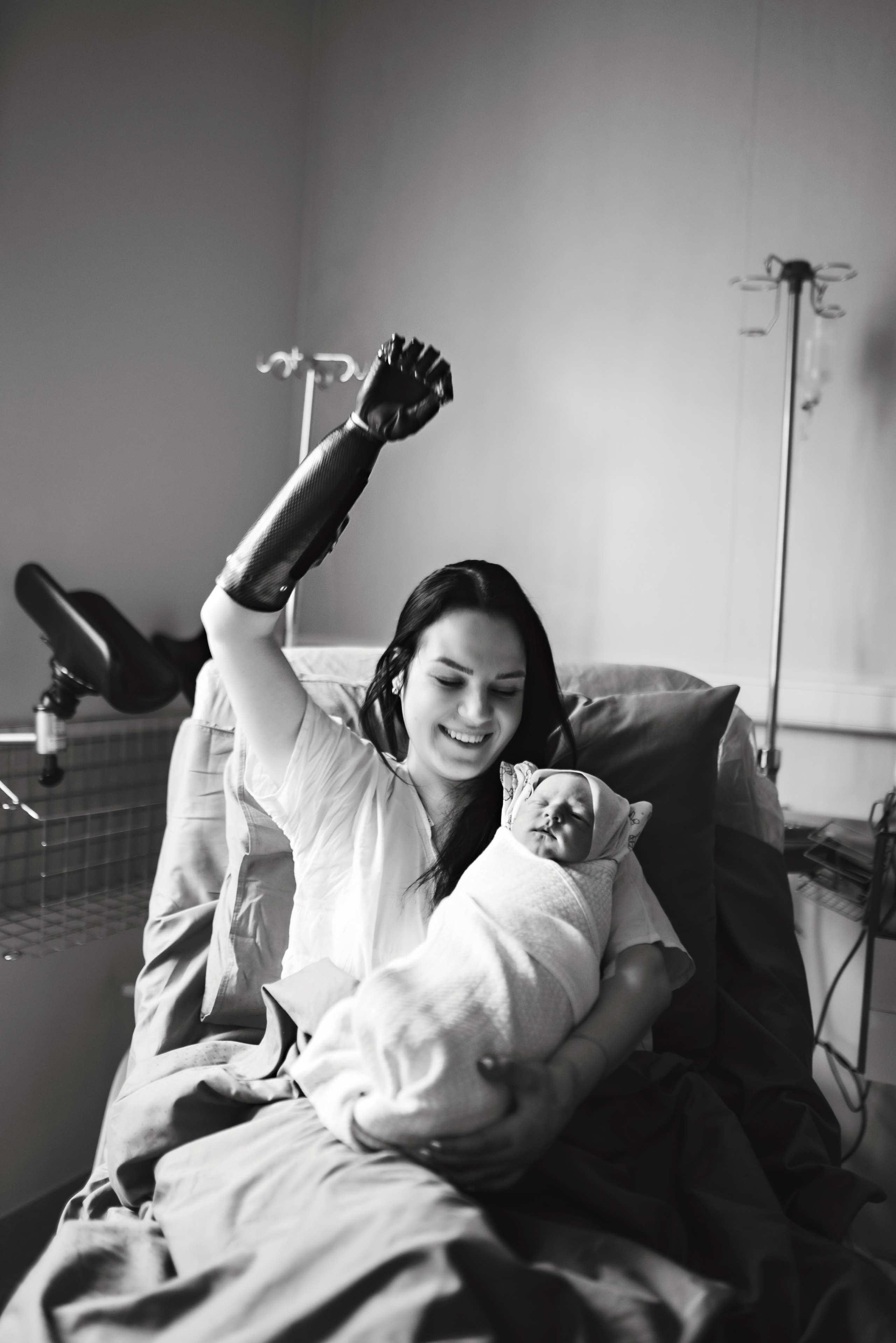 Mother with prosthetic arm holding newborn baby, smiling, captured by Austin birth photographer Anny Smirnova