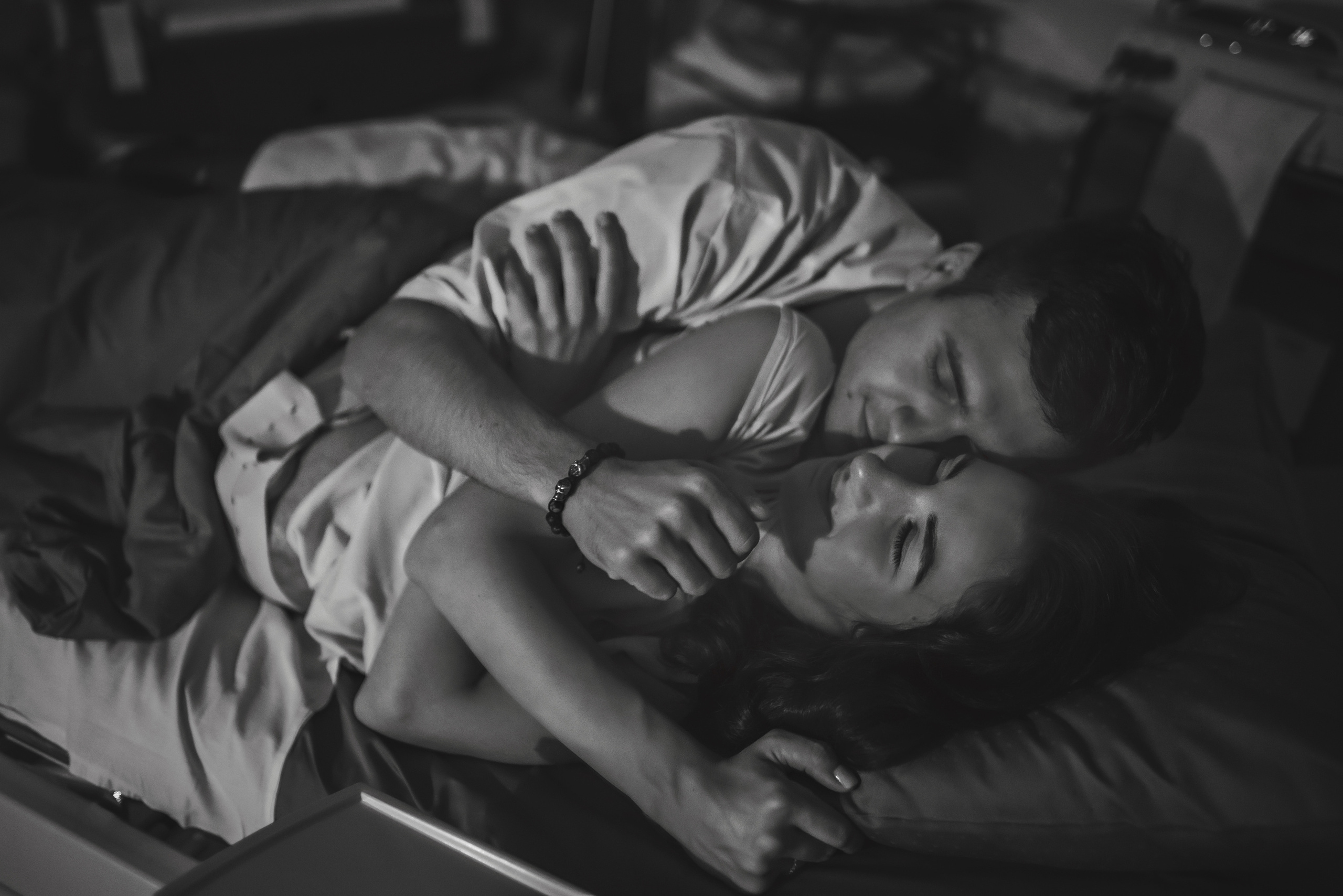 Black and white photo of loving couple embracing in hospital bed after birth. Austin birth photography by Anny Smirnova