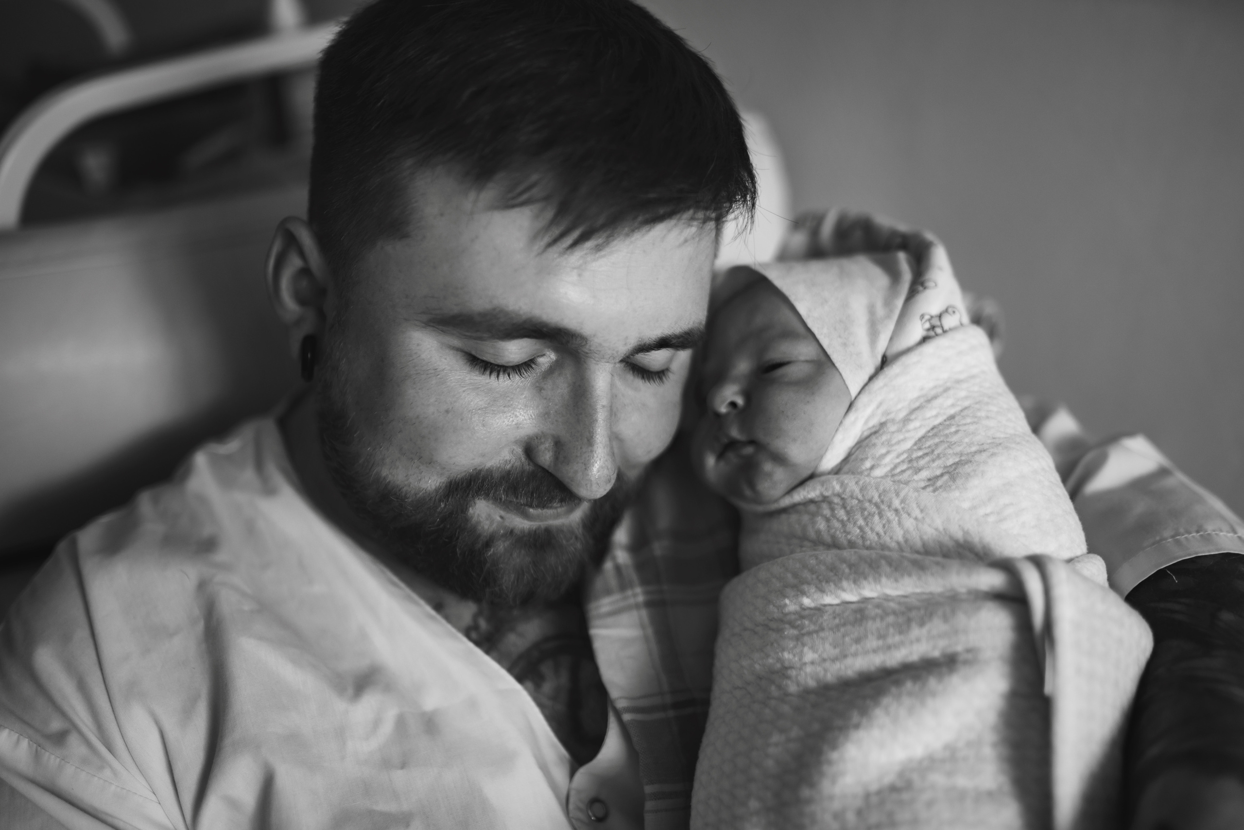 Black and white photo of father gazing at newborn baby in swaddle, taken during birth photography session in Austin, Texas by Anny Smirnova.
