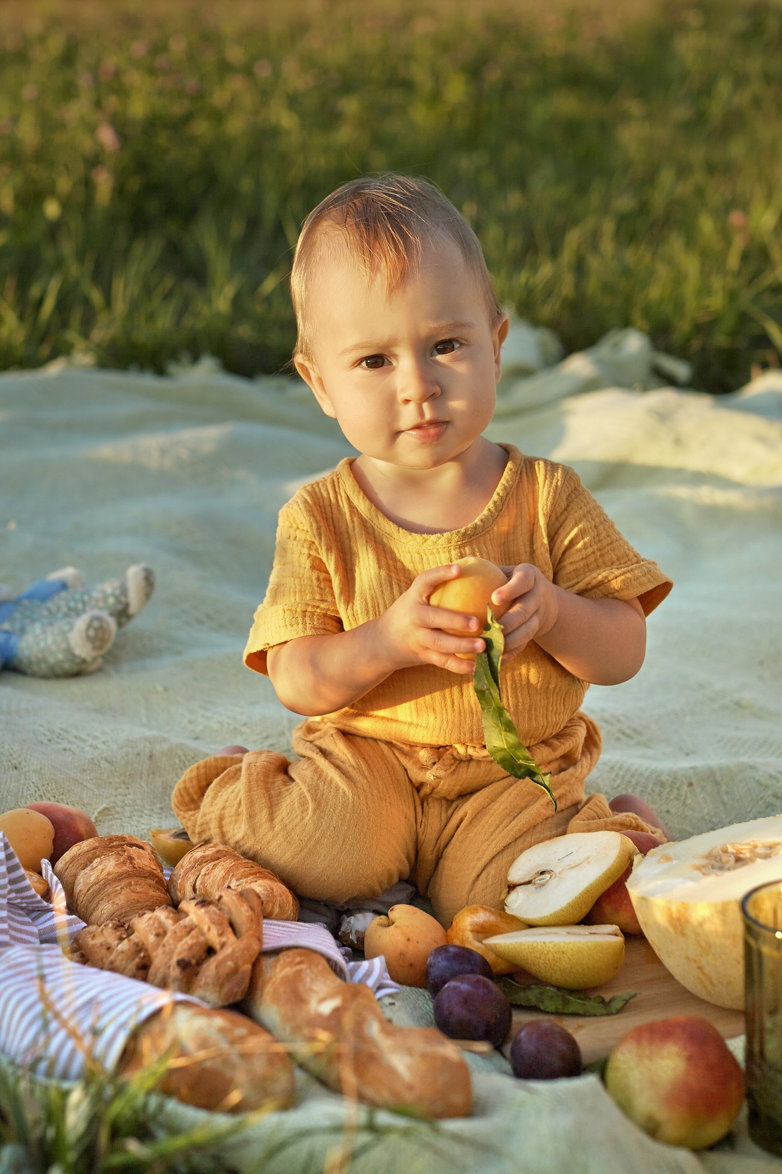 малышка сидит среди фруктов на пикнике в желтом комбинезоне
