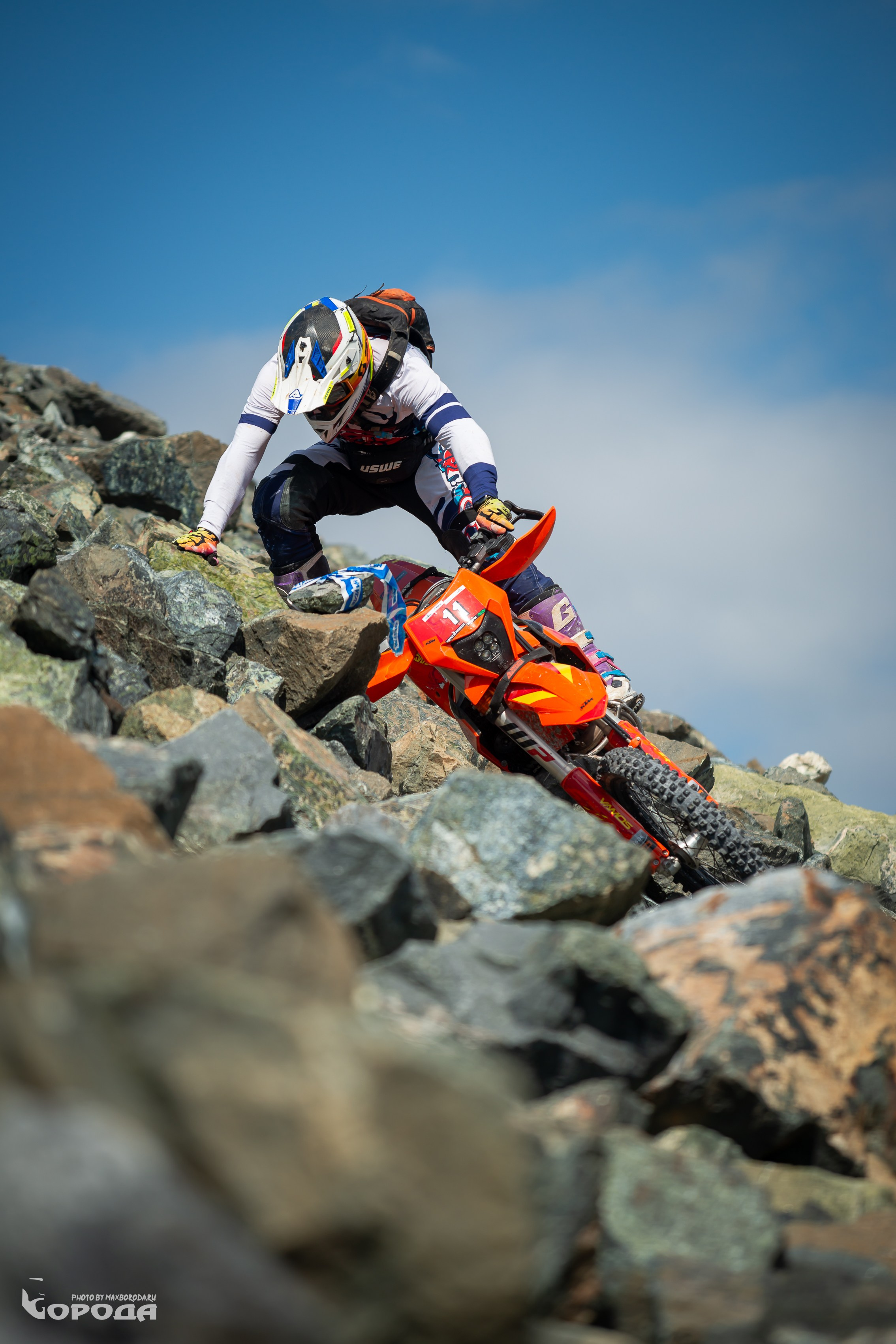 Эндурист в экипировке преодолевает каменистый участок на оранжевом мотоцикле