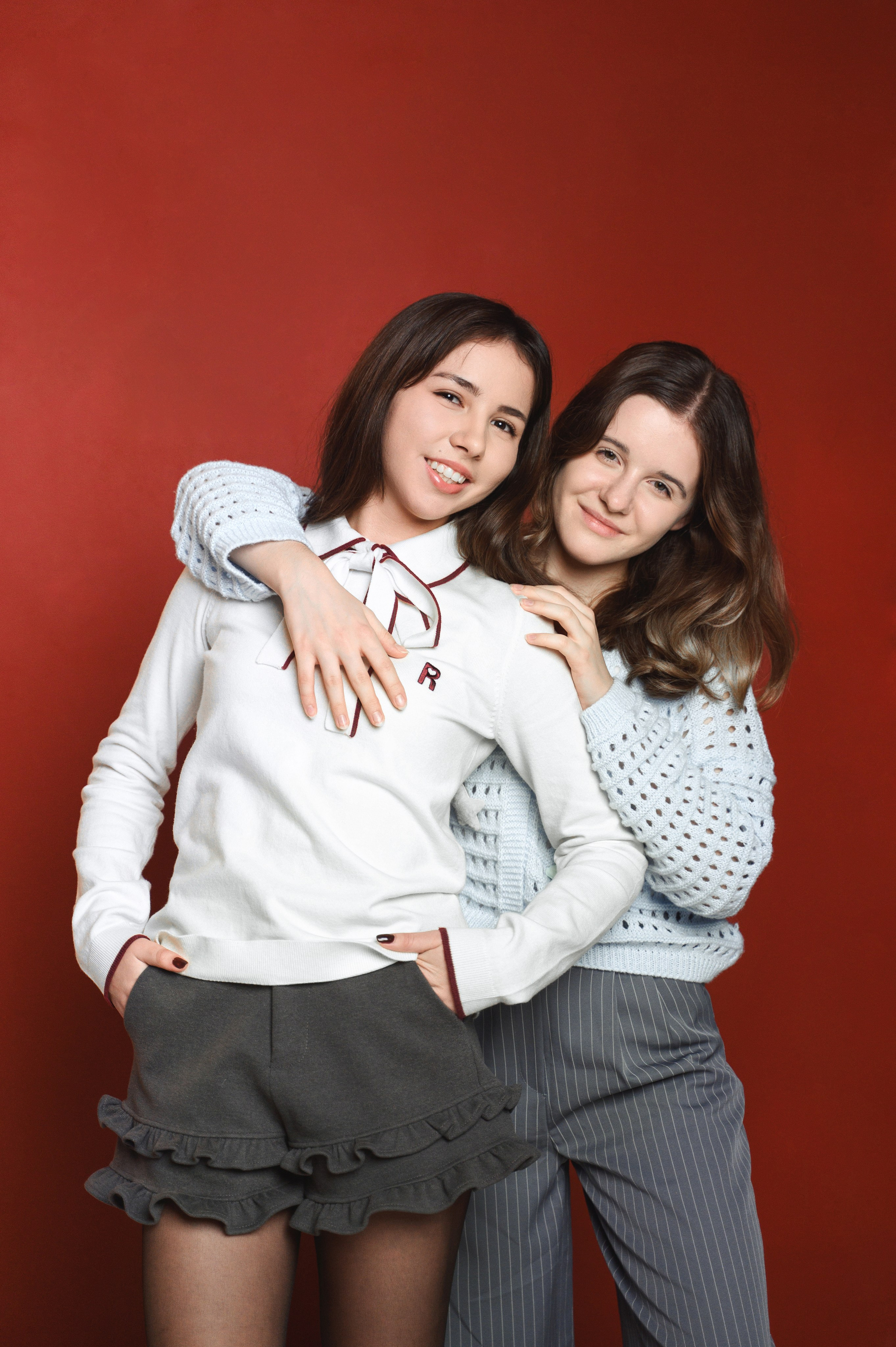 Две подруги обнимаются на красном фоне в студийном кадре для выпускного альбома.