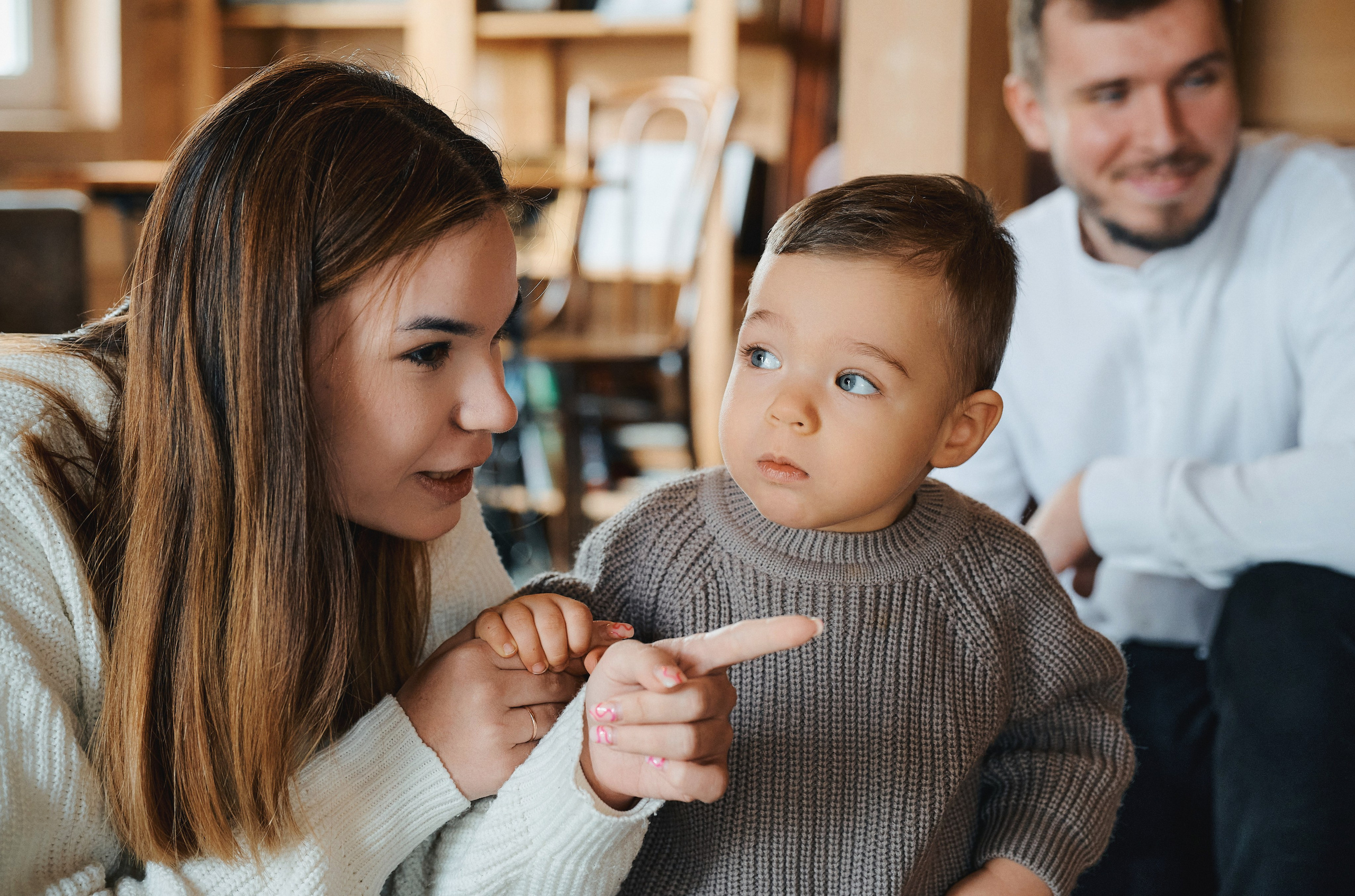 мама и маленький мальчик внимательно смотрят в одну сторону, папа улыбается на заднем плане