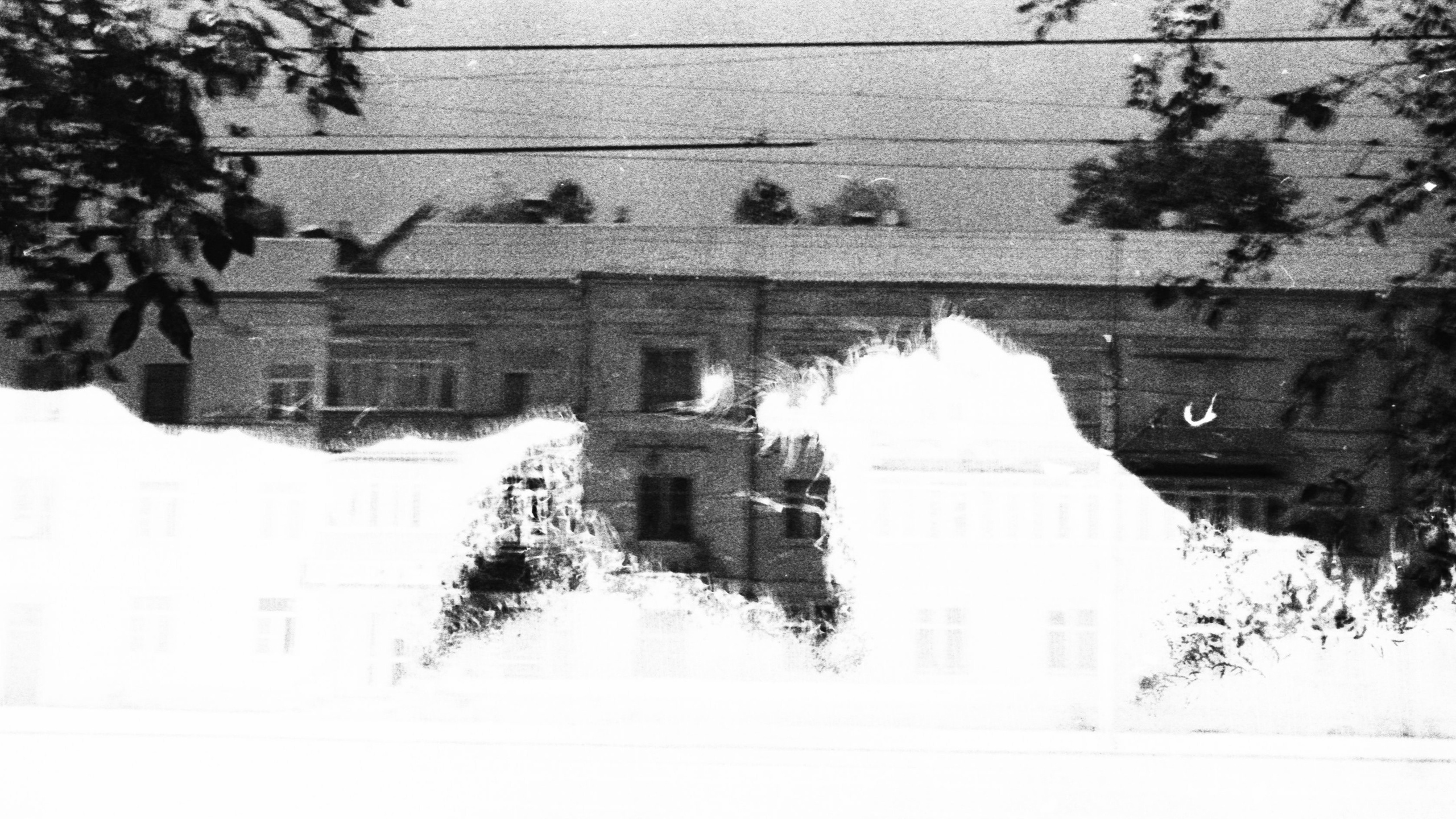 Монохромный городской пейзаж с выраженной засветкой, перепроявлением и эффектом распада плёночного кадра.