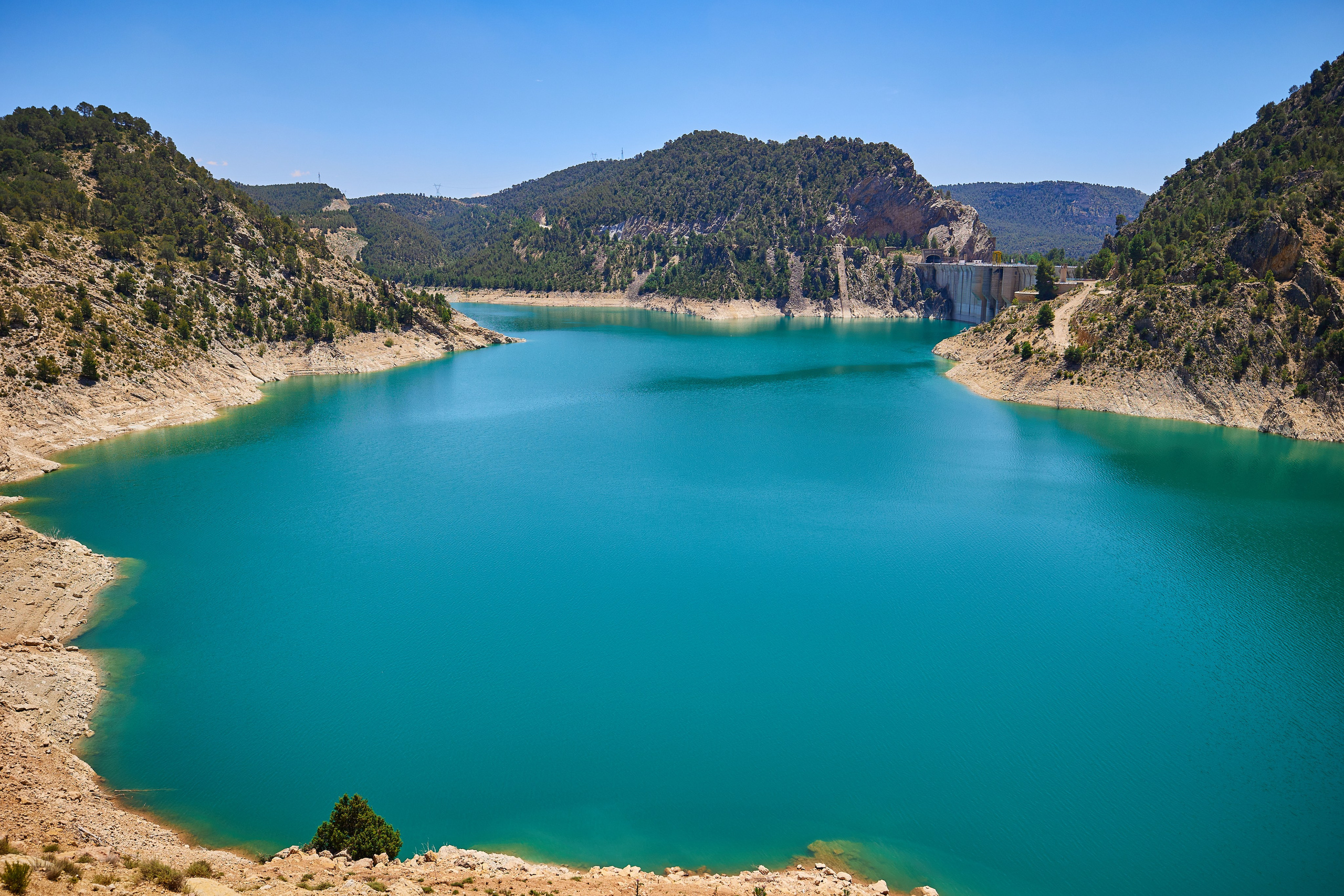 Turquoise waters of the Contreras reservoir surrounded by forested mountains on a sunny day
