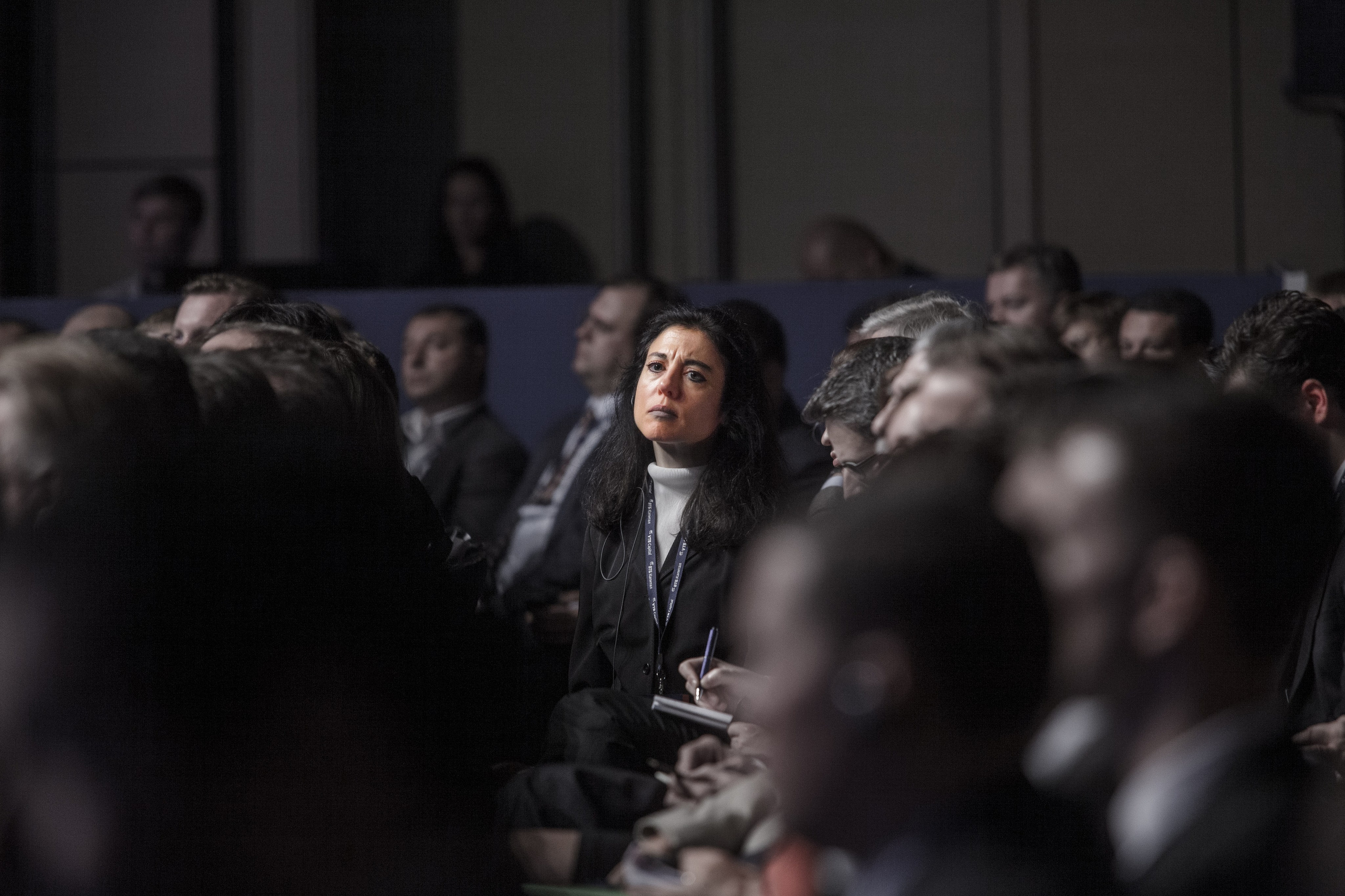 Woman sitting among an audience at a conference or business event, attentive expression, low light, shallow depth of field