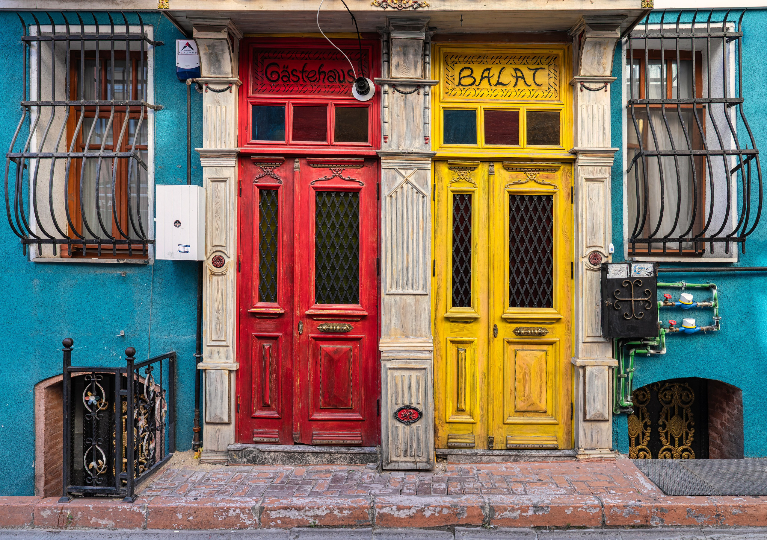 Red and yellow wooden doors of the Balat Gästehaus guesthouse against a blue wall, historic Balat district in Istanbul, Turkish street architecture.