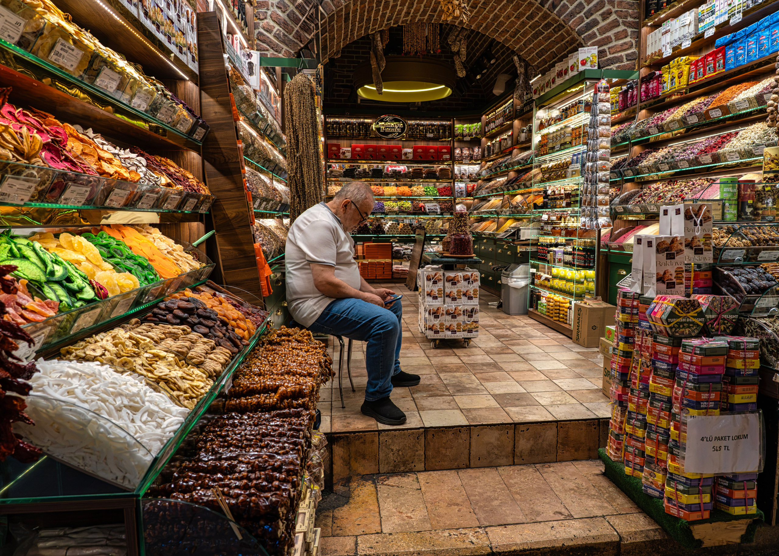 Shopkeeper in a sweet shop at the Grand Bazaar in Istanbul, shelves with Turkish delight and dried fruits, street photography.
