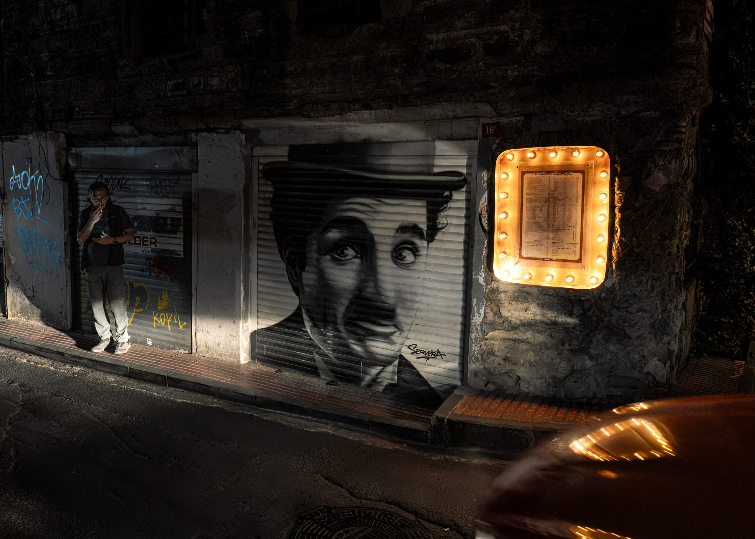 Night Istanbul, Charlie Chaplin graffiti on shutters, vintage light bulb frame, street art.