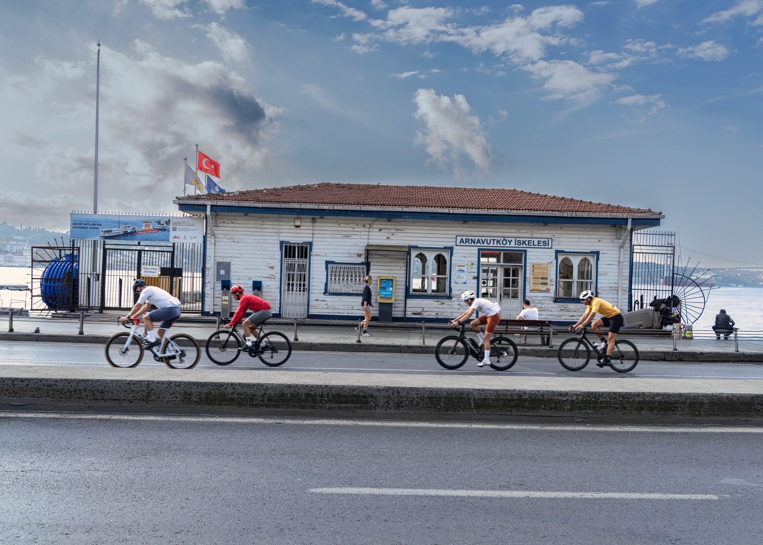 Arnavutköy Pier on the Bosphorus, cyclists by a white building, Istanbul street photography.