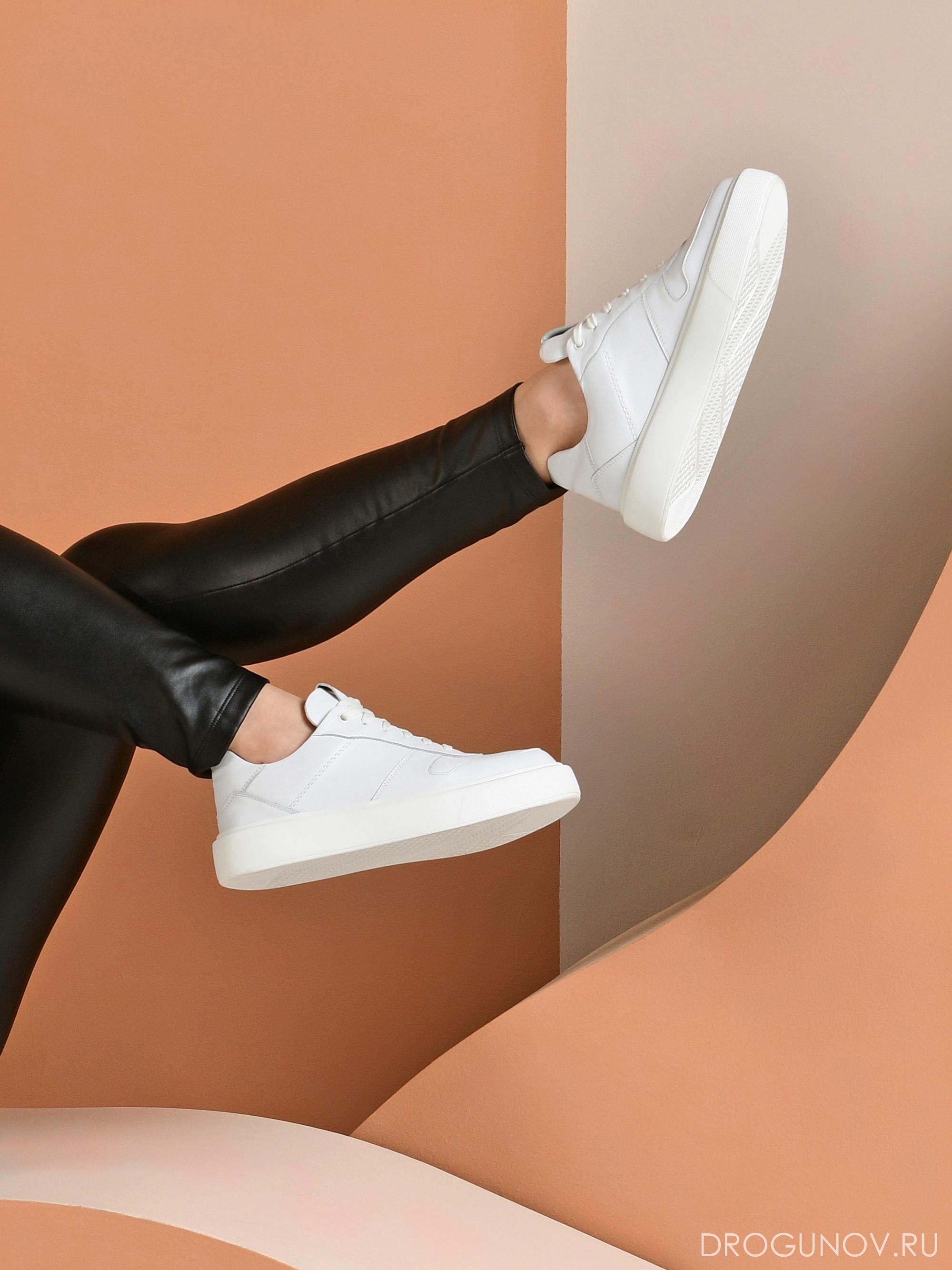 Белые кроссовки на ногах на оранжевом фоне.