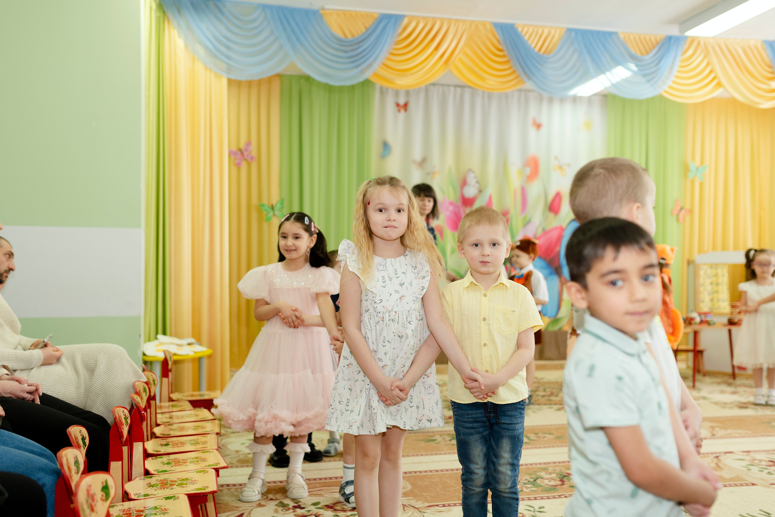 Дети танцуют веселый танец в праздничных костюмах на утреннике 8 марта в детском саду.