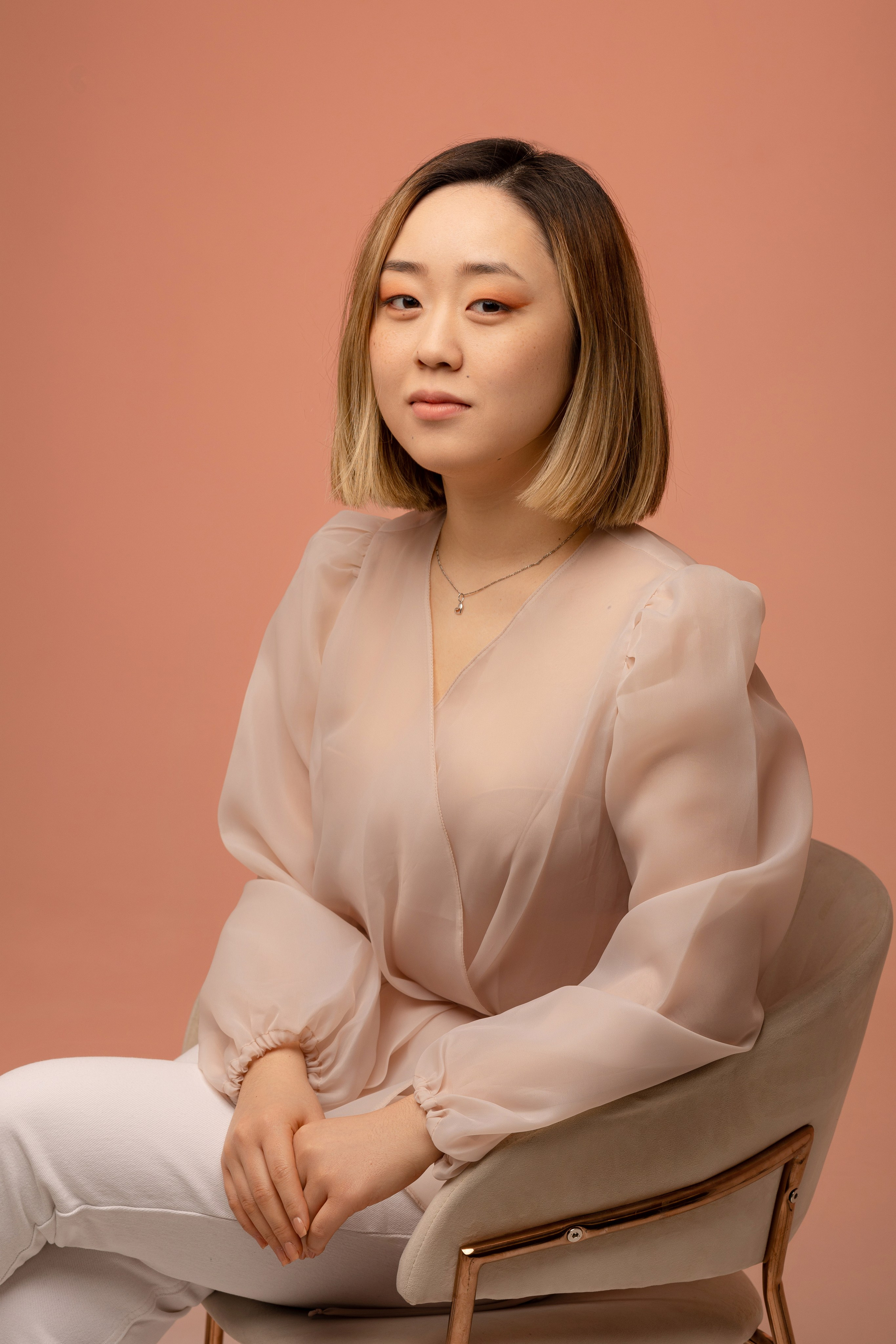 Девушка сидит в кресле в пол оборота, соединив руки над левым коленом.