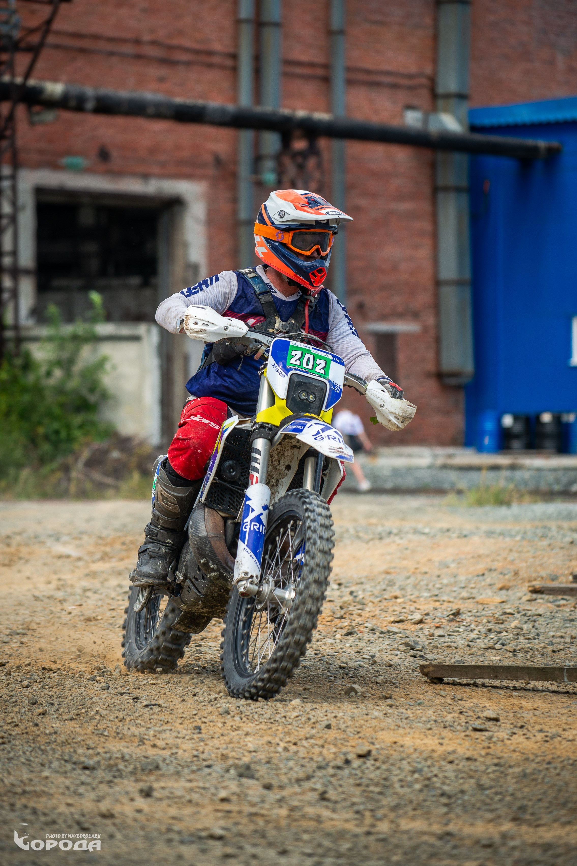 Эндурист в оранжево-синем шлеме едет по пересечённой местности.