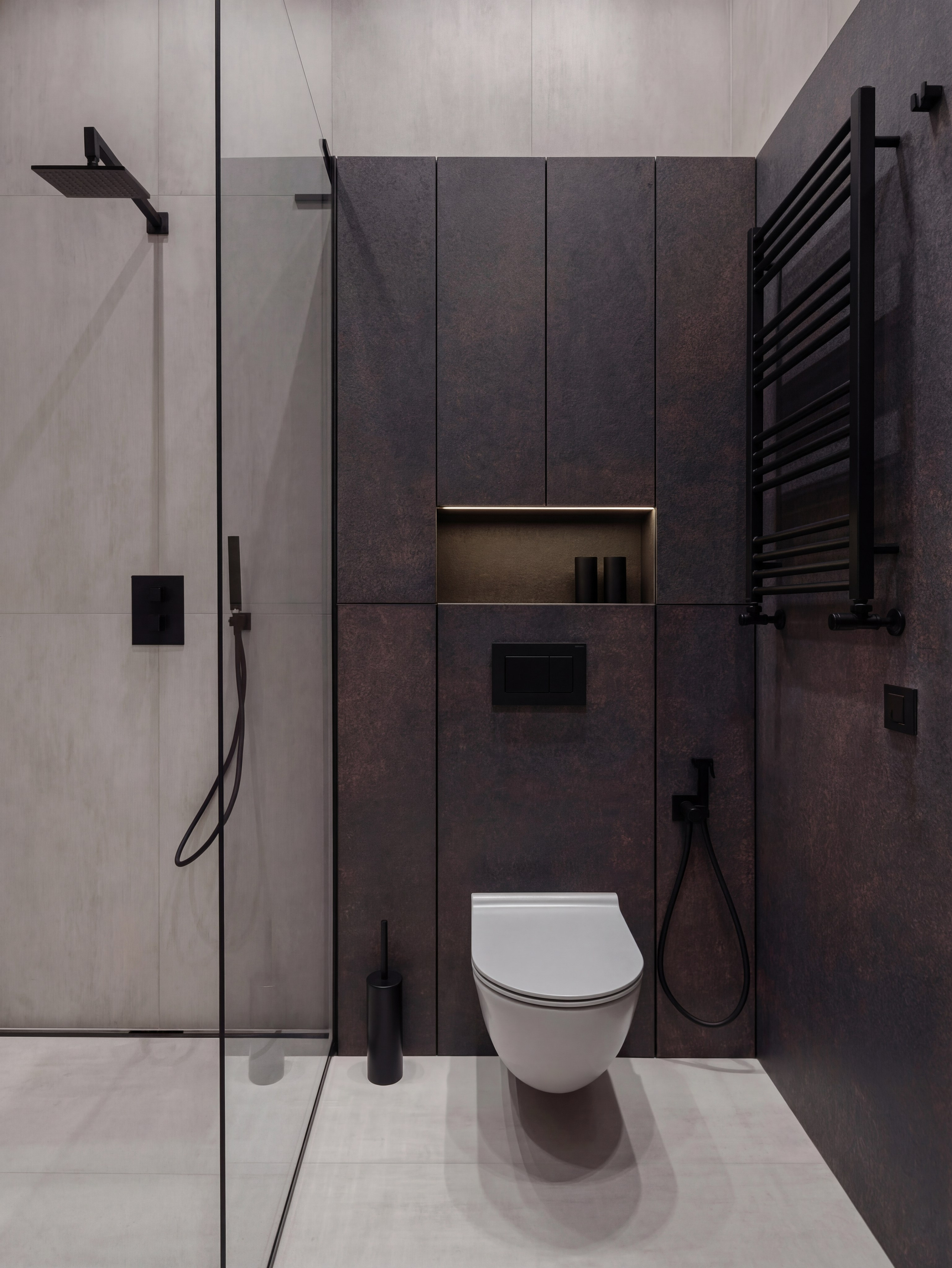 Минималистичный интерьер санузла от Валерии Котович: инсталляция унитаза на фоне темных панелей под металл, встроенная ниша с подсветкой, черная душевая система и отделка под бетон в доме у воды.