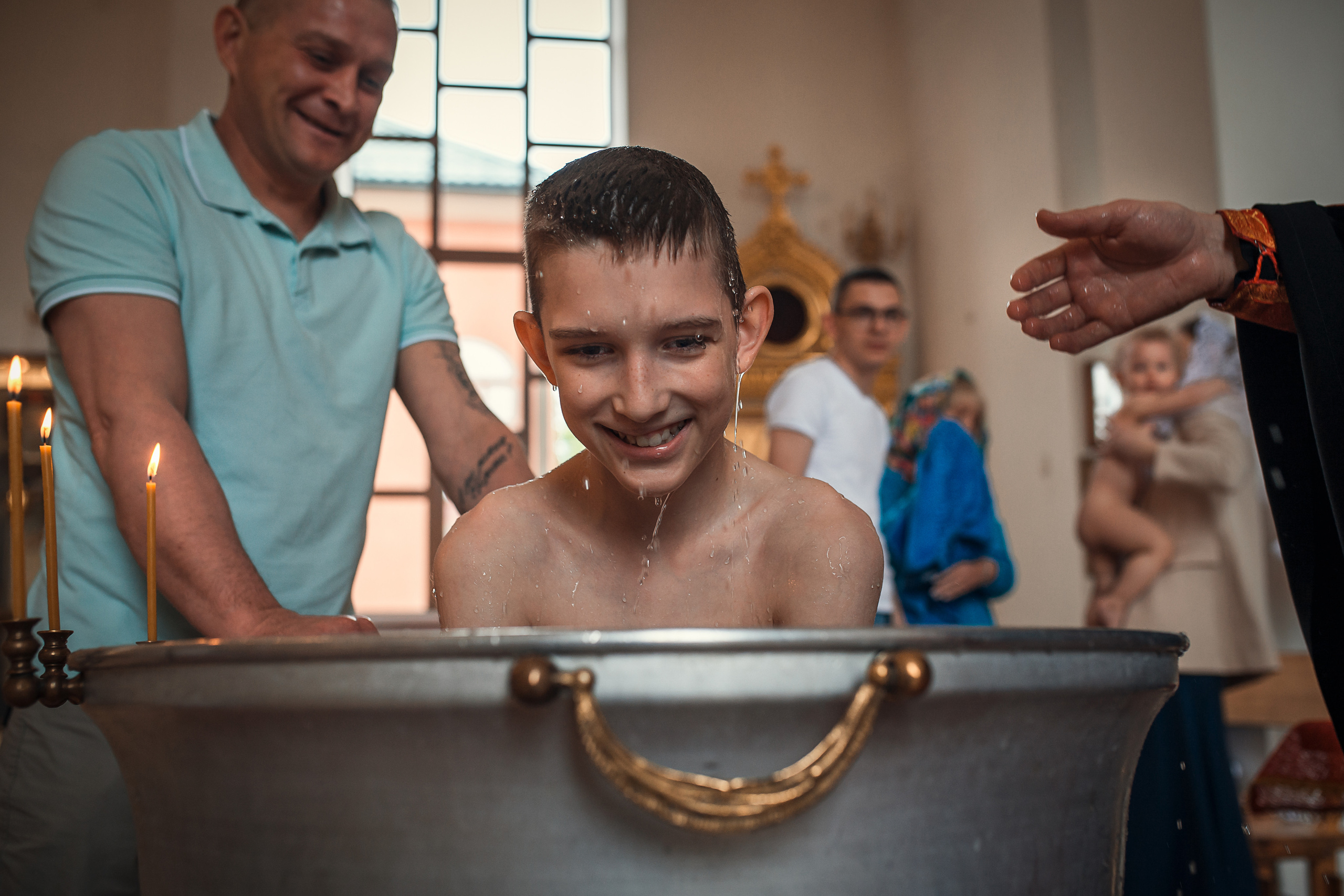 Мальсик в купели, на него летят брызки святой воды.Он крестится.Крещение.