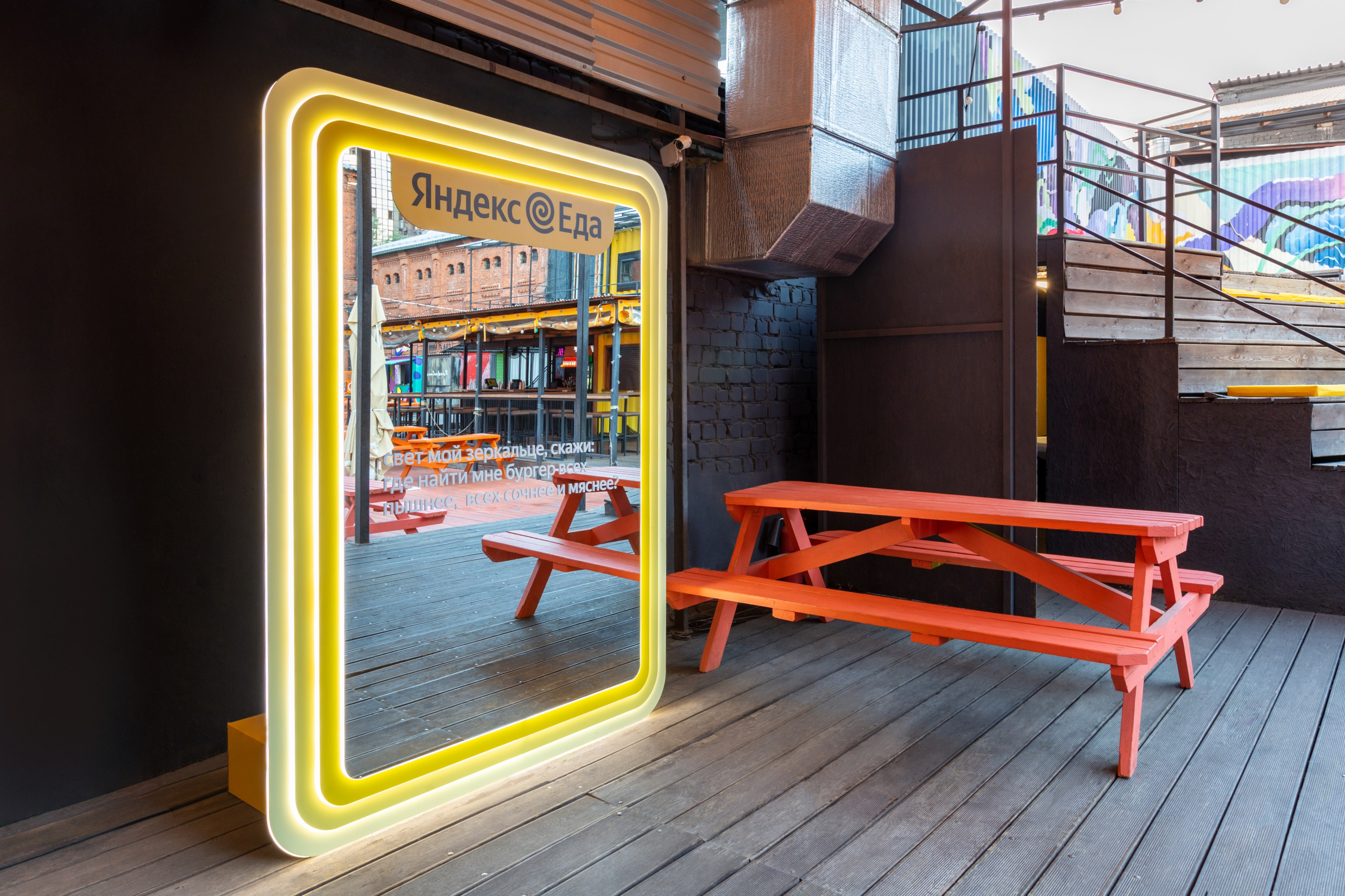 Желтое зеркало с подсветкой рядом с красной скамейкой на деревянном полу.