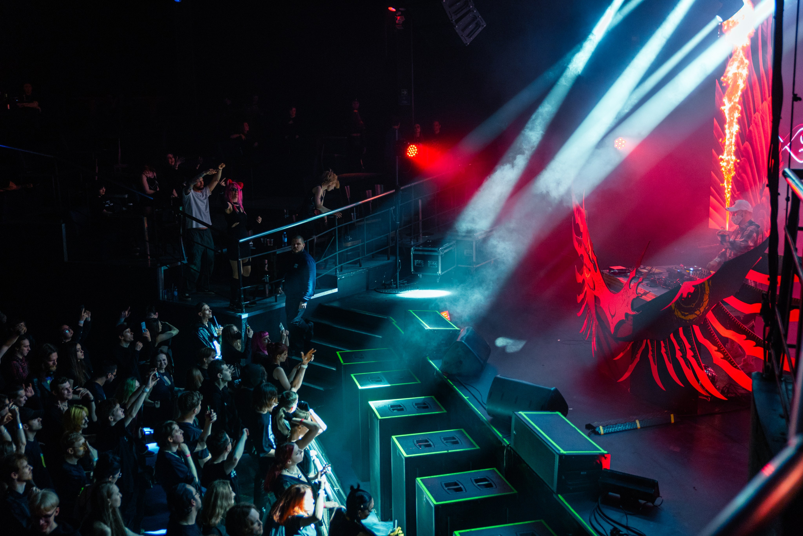 Музыкальный фестиваль РАСПАД 2, в кадре сцена и зрители, ракурс сбоку, на сцене красный свет, синие прожекторы светят на людей в зале