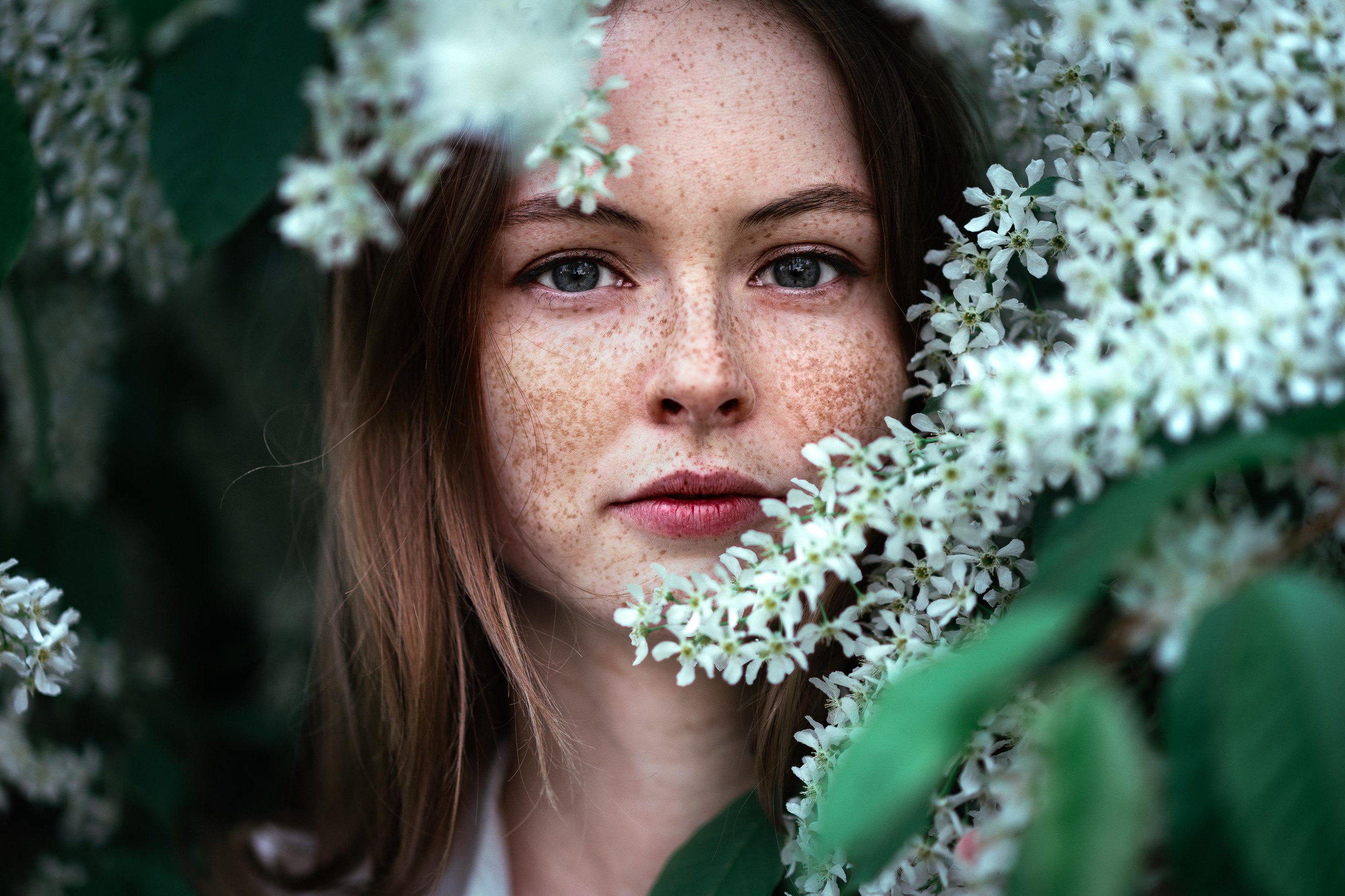 portrait of a red-haired girl with freckles with green eyes in bird cherry flowers