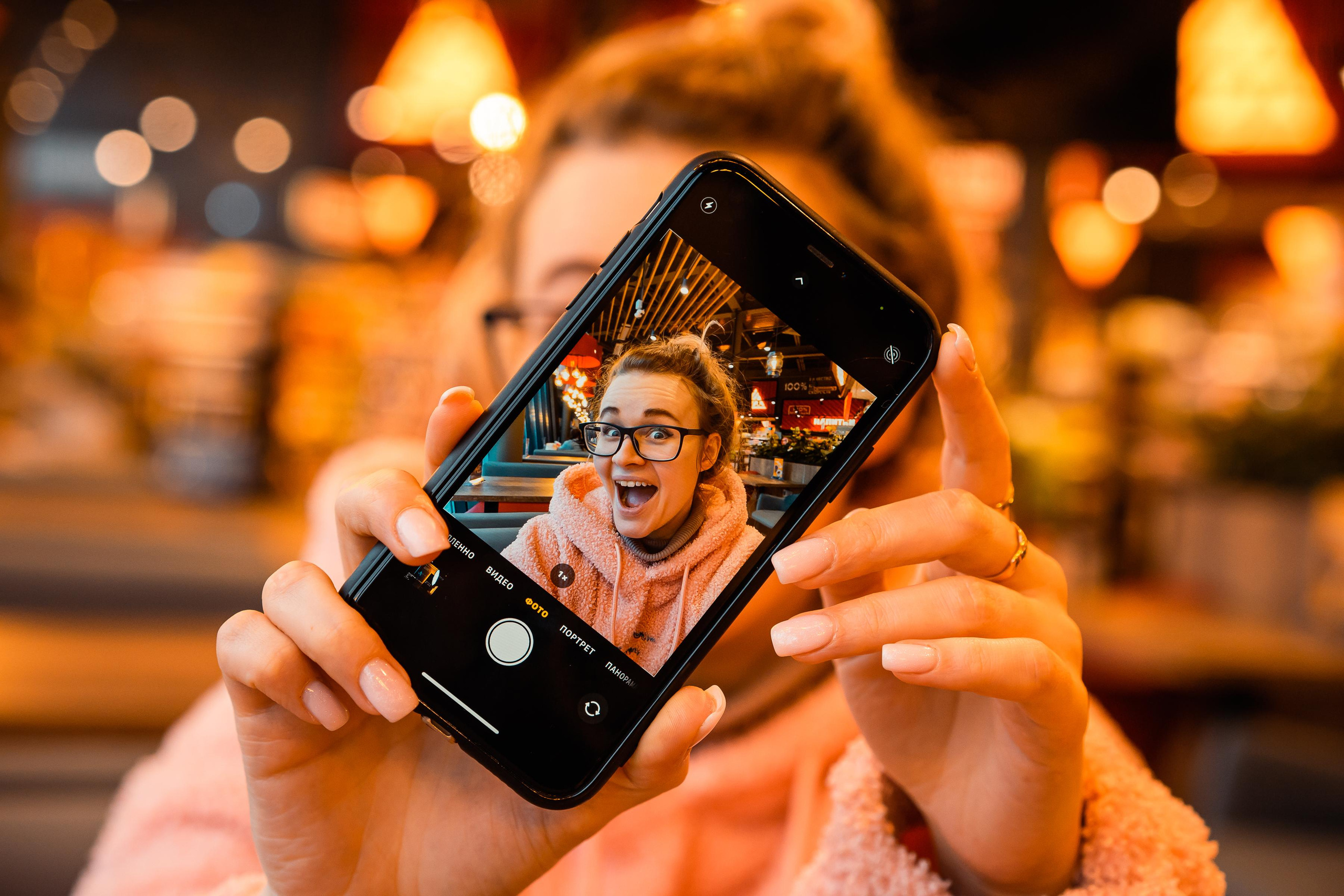 juicy photo in orange tones of a girl in glasses taken through the screen of the phone