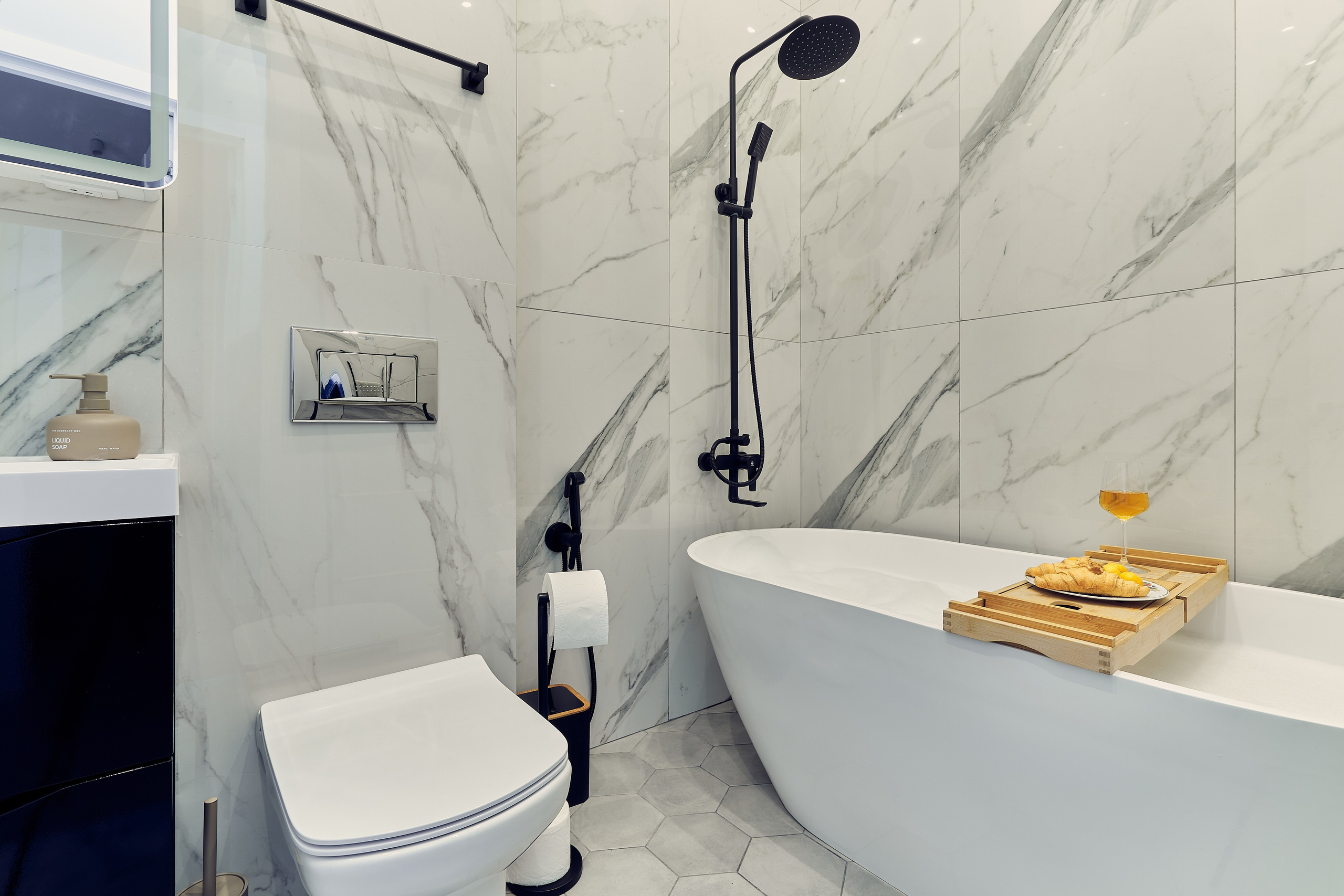 Интерьерное фото санузла в апартаментах в Москве с наполненной ванной, двумя круассанами и бокалом с напитком