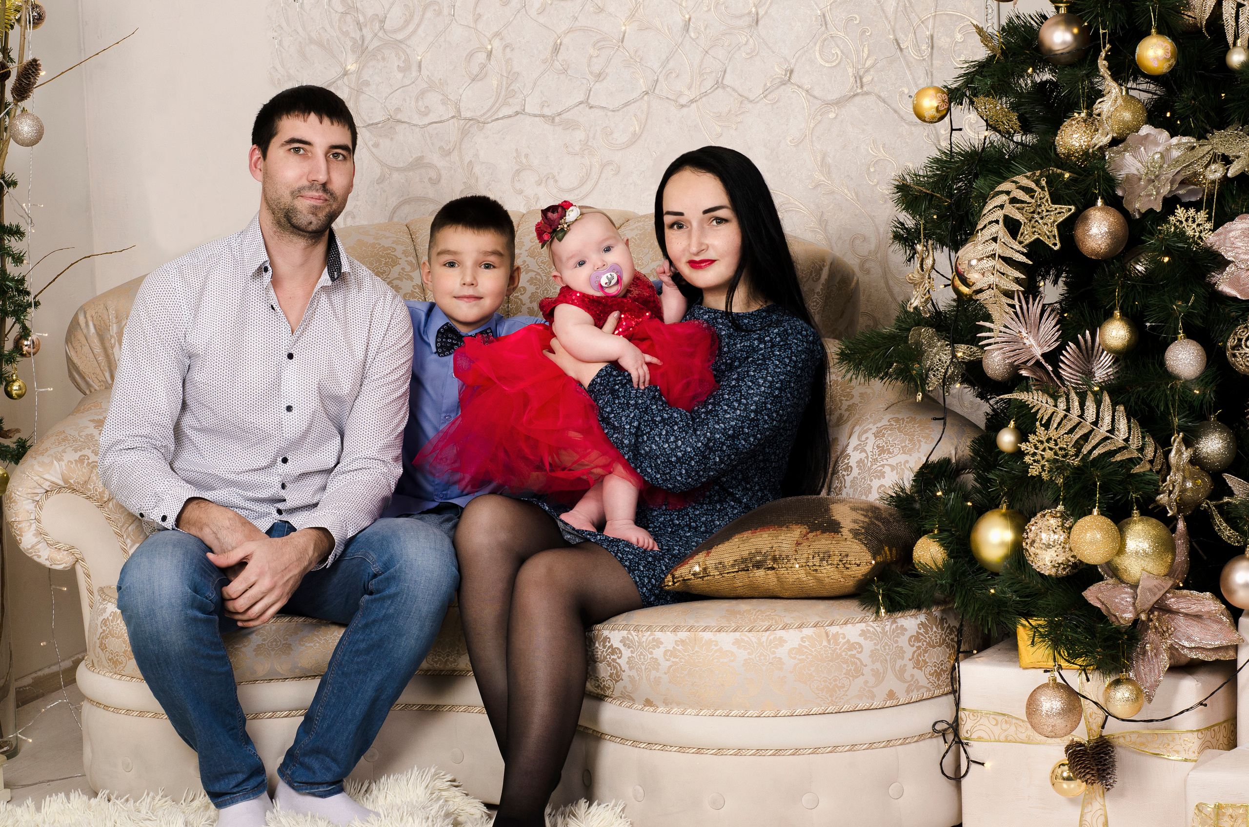 Семья из четырех человек на диване, рядом с елкой.