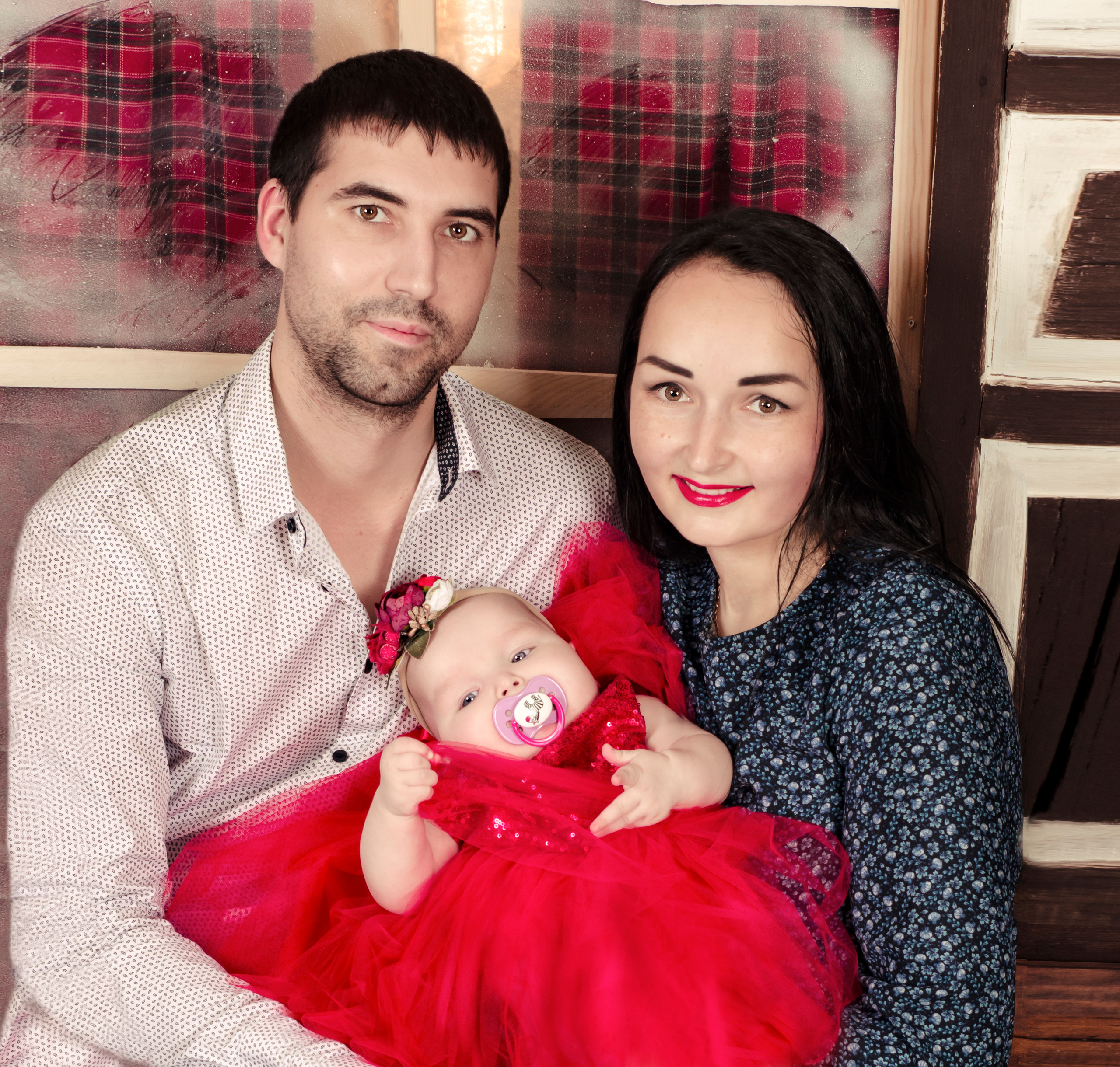 Папа, мама и маленькая девочка на фоне замороженного окна.