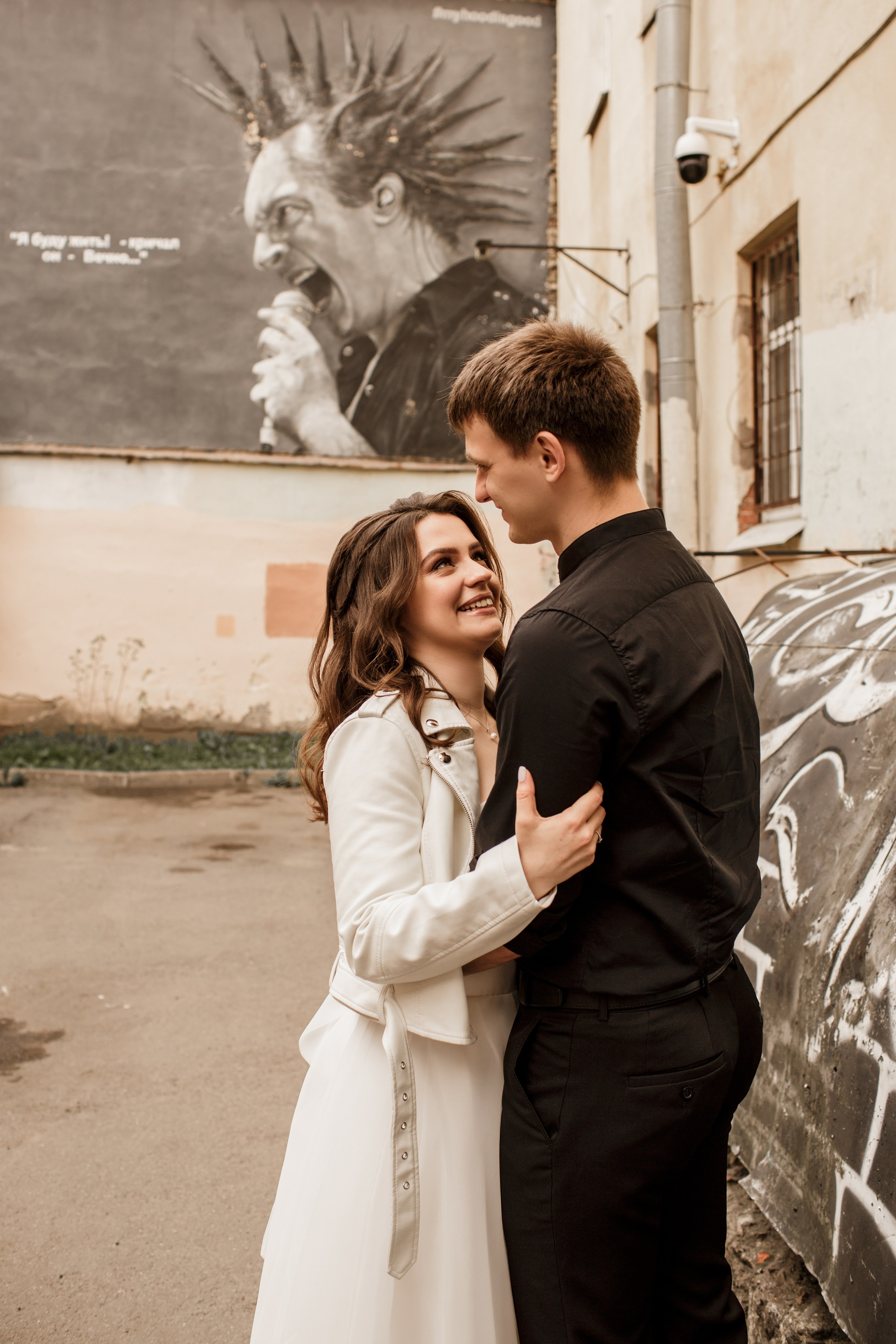 Жених и невеста нежно смотрят друг на друга на фоне граффити Михаила Горшка Горшенева в Санкт-Петербурге.