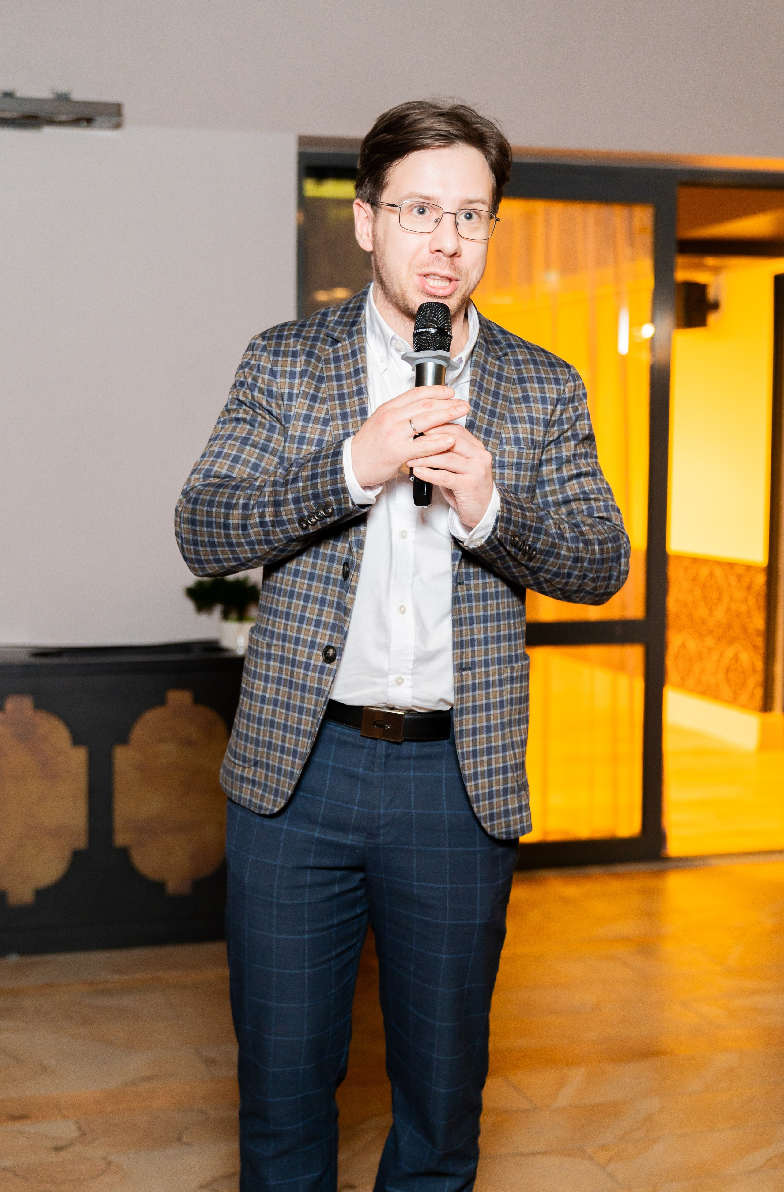 Мужчина в клетчатом пиджаке выступает с микрофоном на корпоративном мероприятии в Radisson Sonya. Фото Евгения Мальцева.