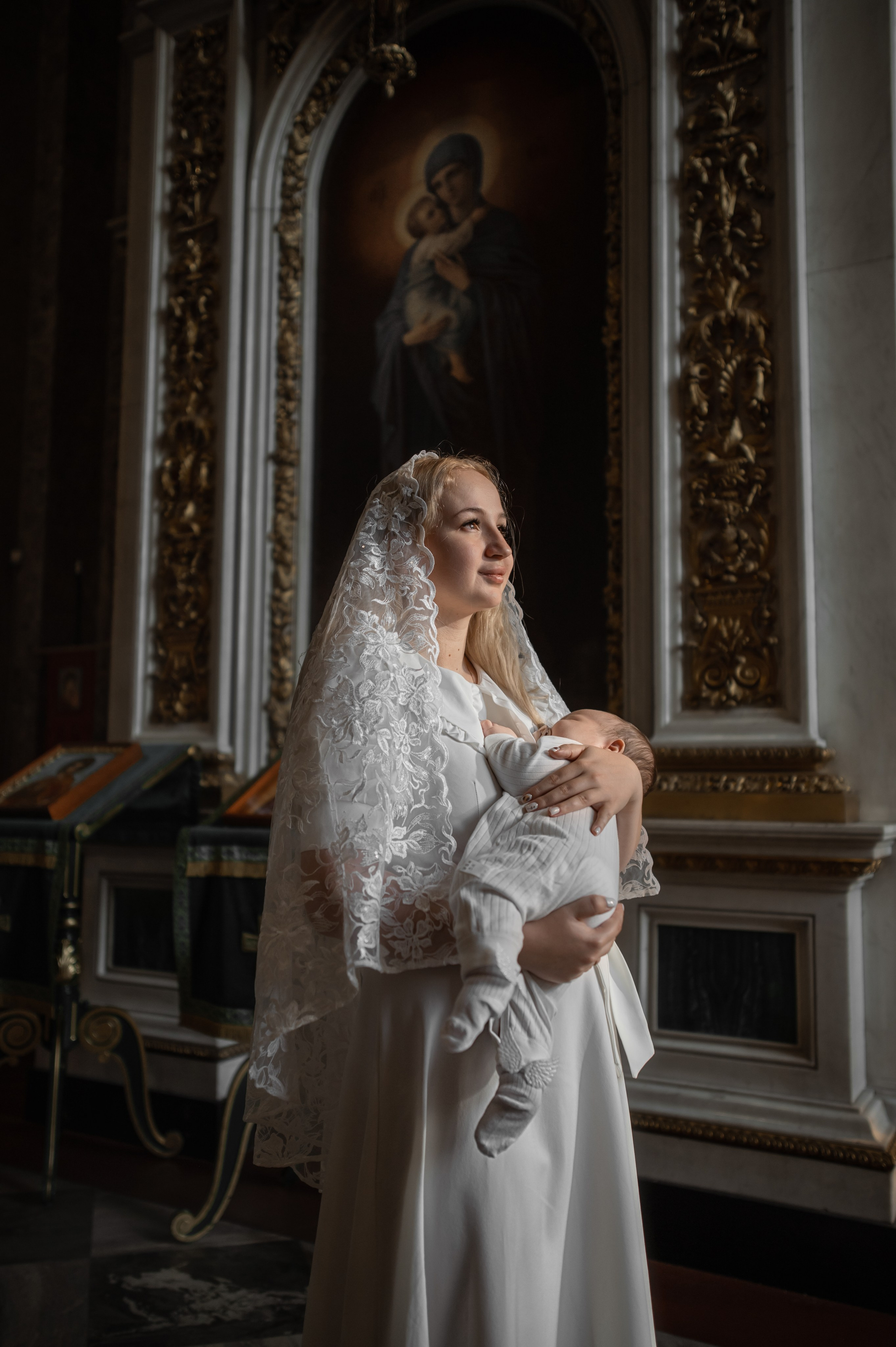 мать держит спящего младенца на руках на фоне иконы Богородицы в Исаакиевском соборе