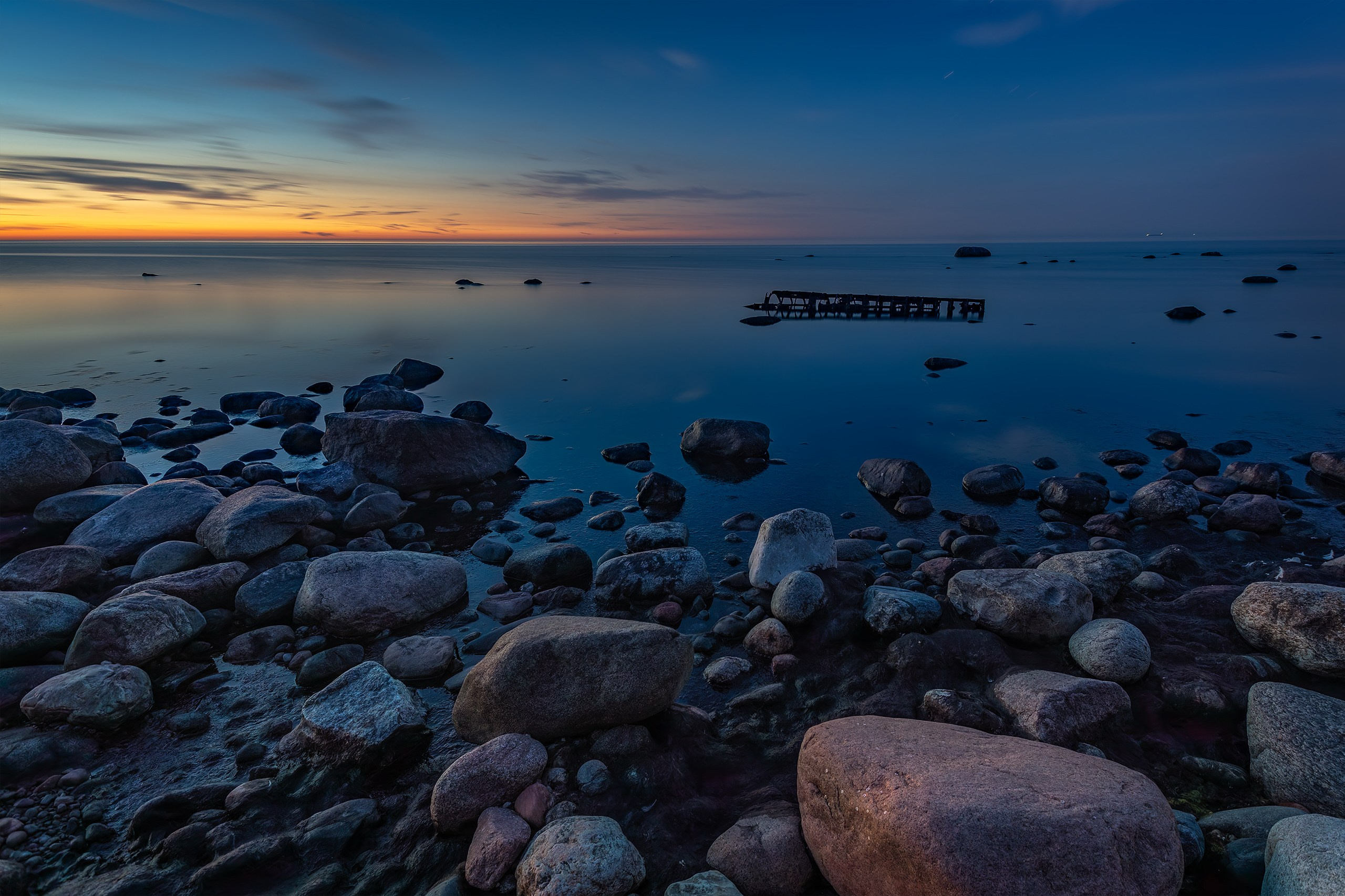 Midnight twilight over a stony Baltic sea shore with distant rusted remains of a sunken barge near Wachbude.