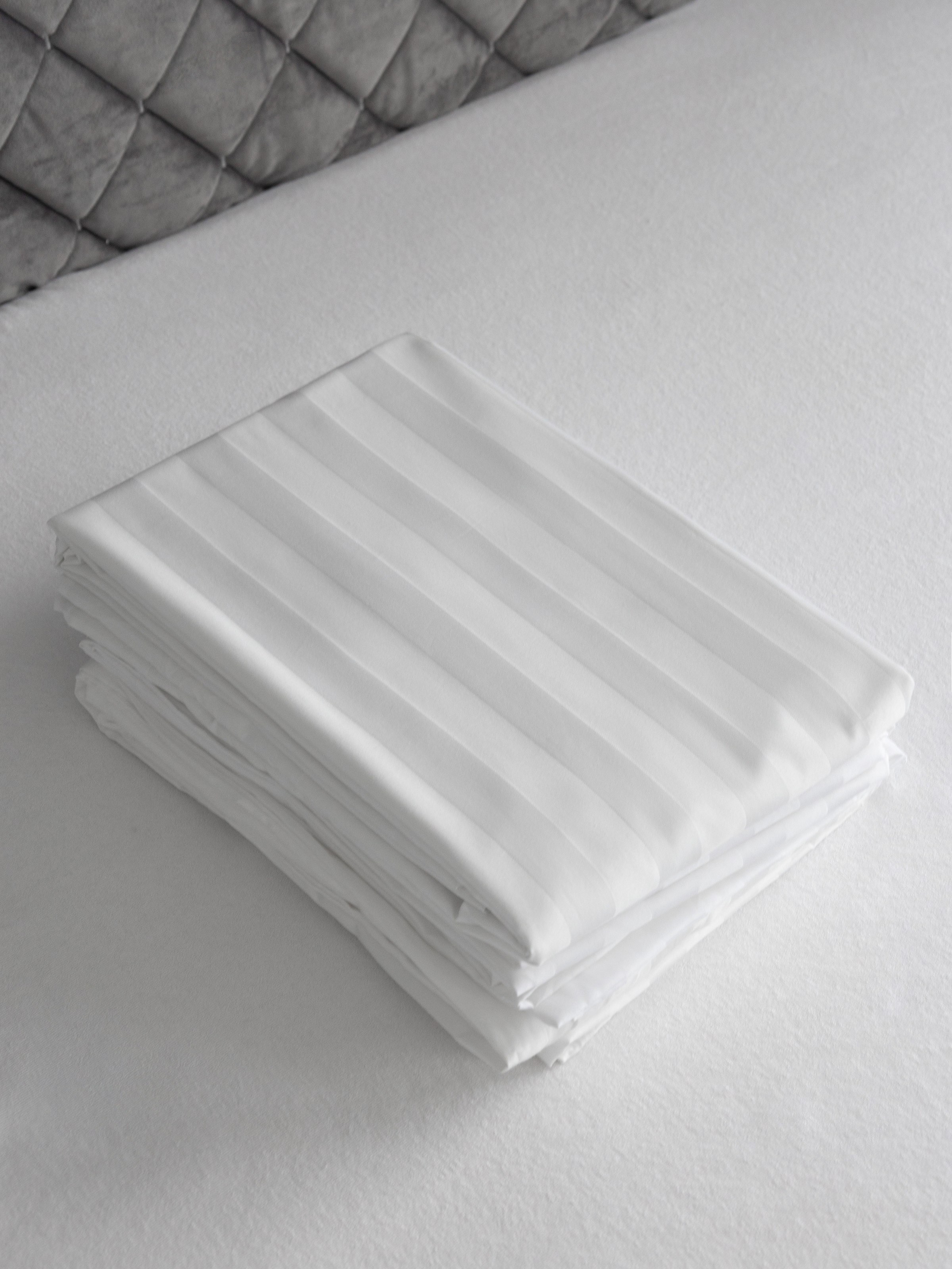 Аккуратно сложенная простынь с узором страйп на кровати | Фото для каталога текстиля