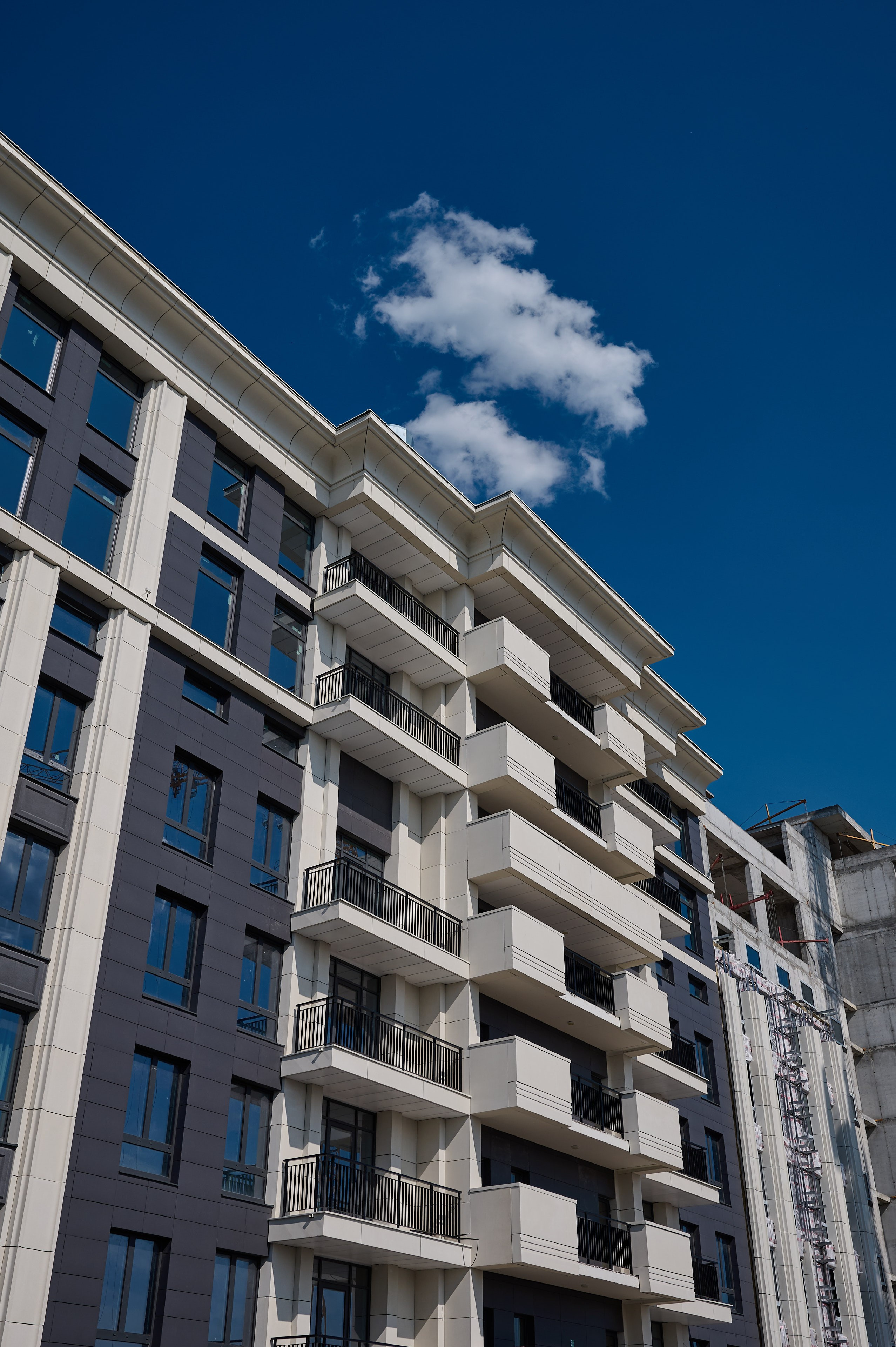 Современное многоэтажное здание с архитектурными деталями в классическом стиле — белыми карнизами, балконами и синим небом с облаками на фоне