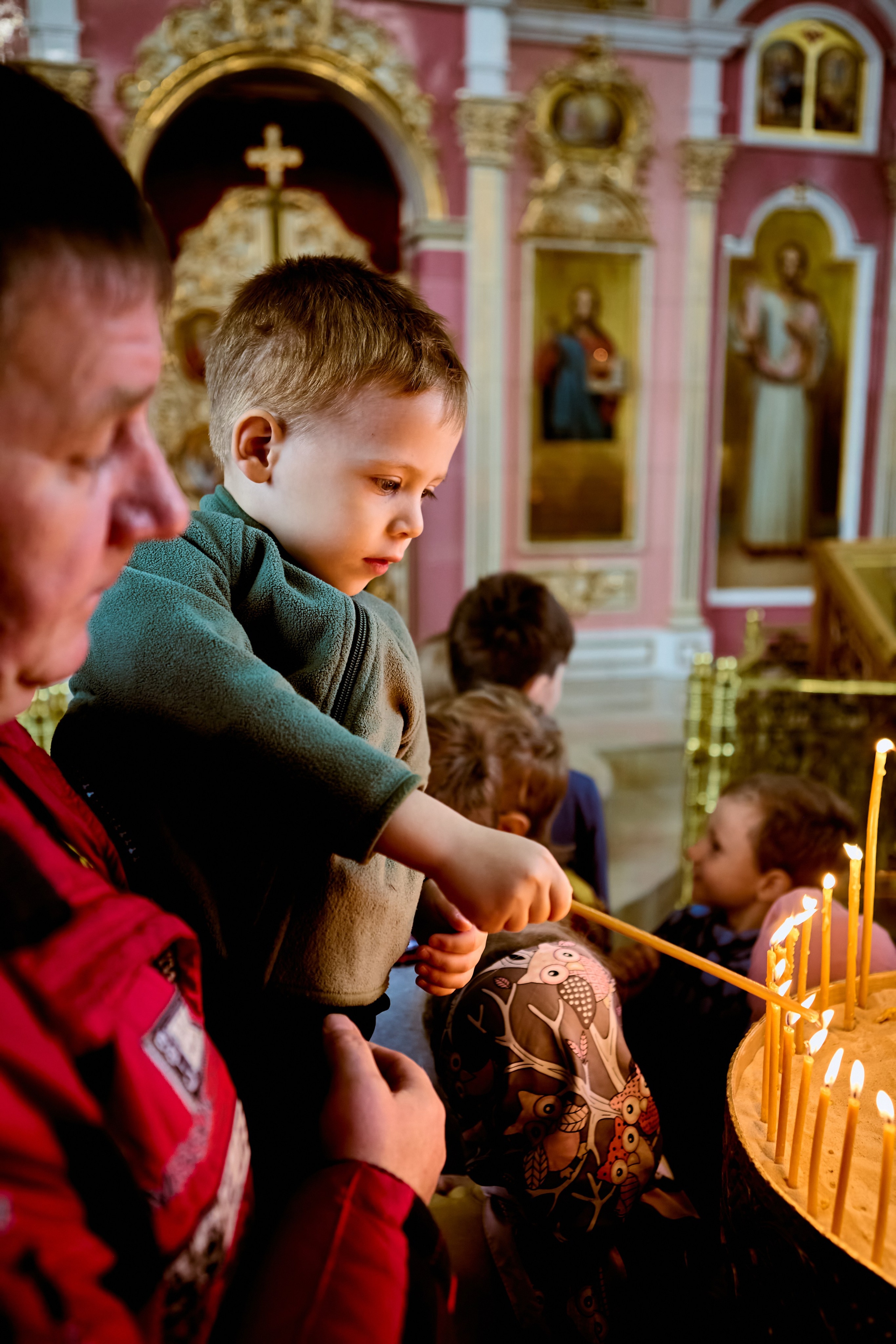 У подсвечника малыш на руках у папы возжигает свечу 