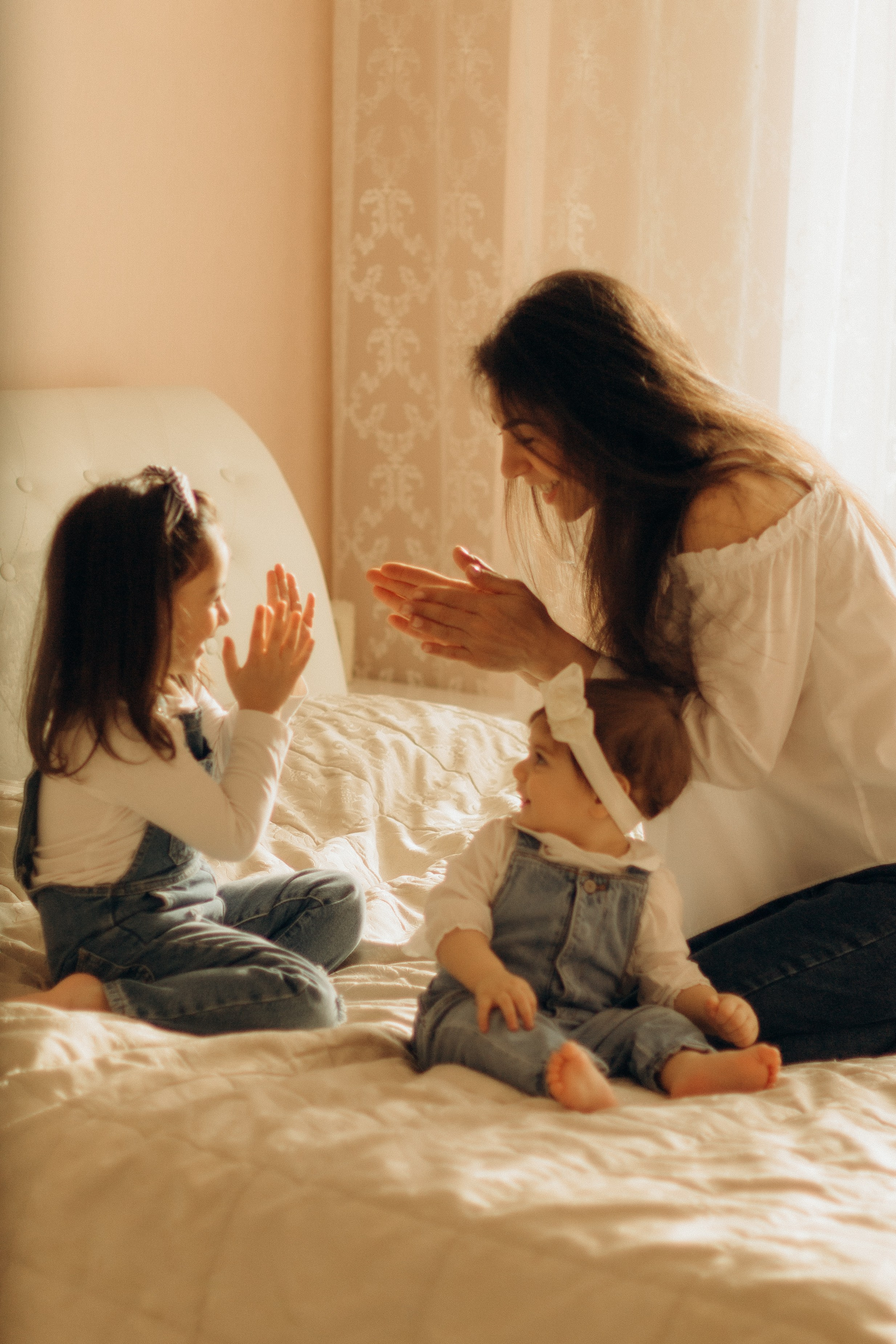 Семейная фотосессия мамы и двух дочек,  мама с дочками играет на кровати